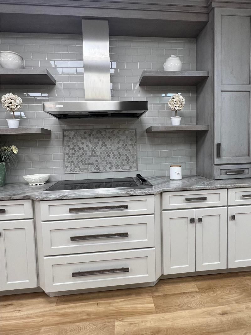 Gray and white kitchen with stainless steel range hood, floating shelves, and cabinets.