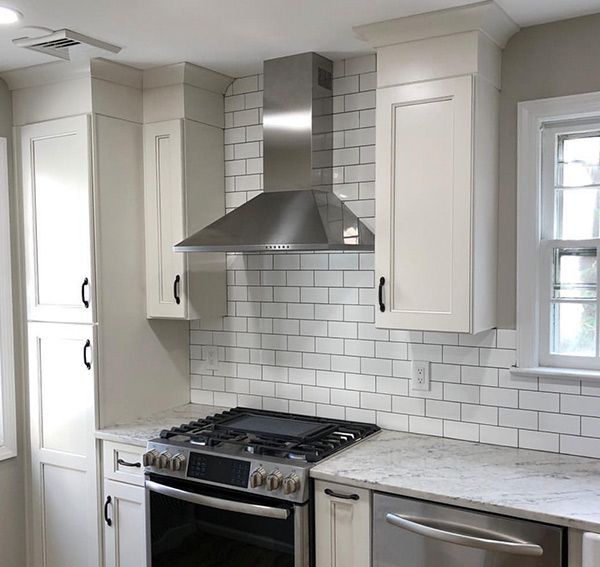 Kitchen with white cabinets, stainless steel range hood, white subway tile backsplash, and a gas range.