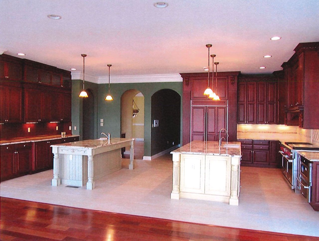 Spacious kitchen with dark wood cabinets, two light-colored islands, and pendant lights.