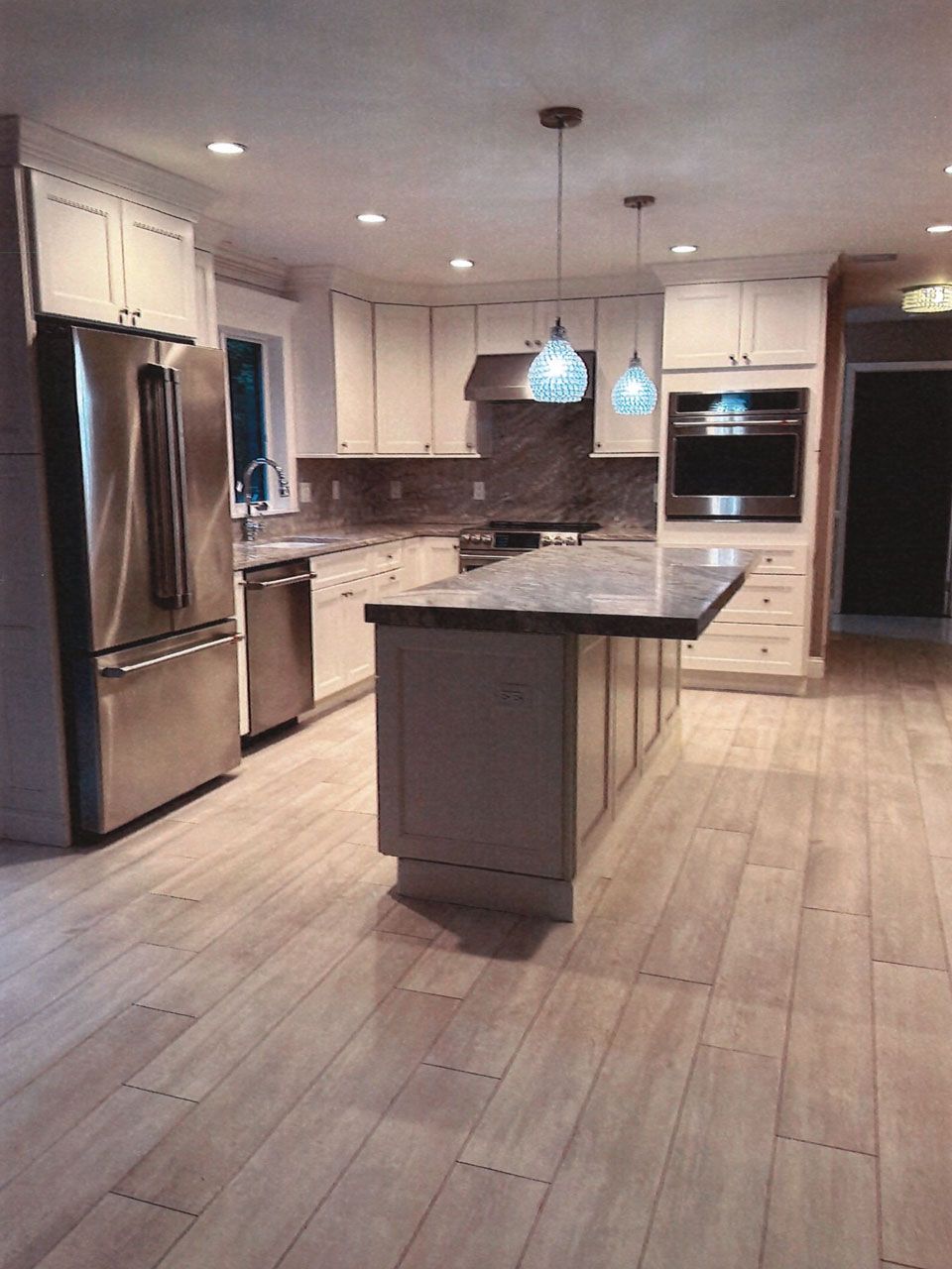 Modern kitchen with light wood floor, white cabinets, stainless steel appliances, and a gray countertop island.