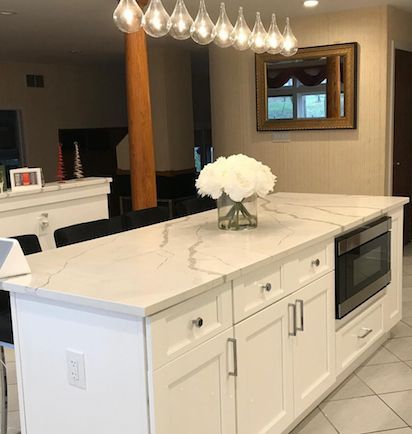 White kitchen island with marble-look countertop, built-in microwave, white cabinets, and overhead light.