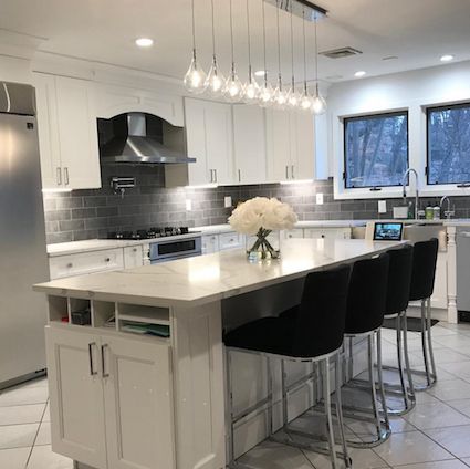 Modern white kitchen with island, gray backsplash, and black bar stools.
