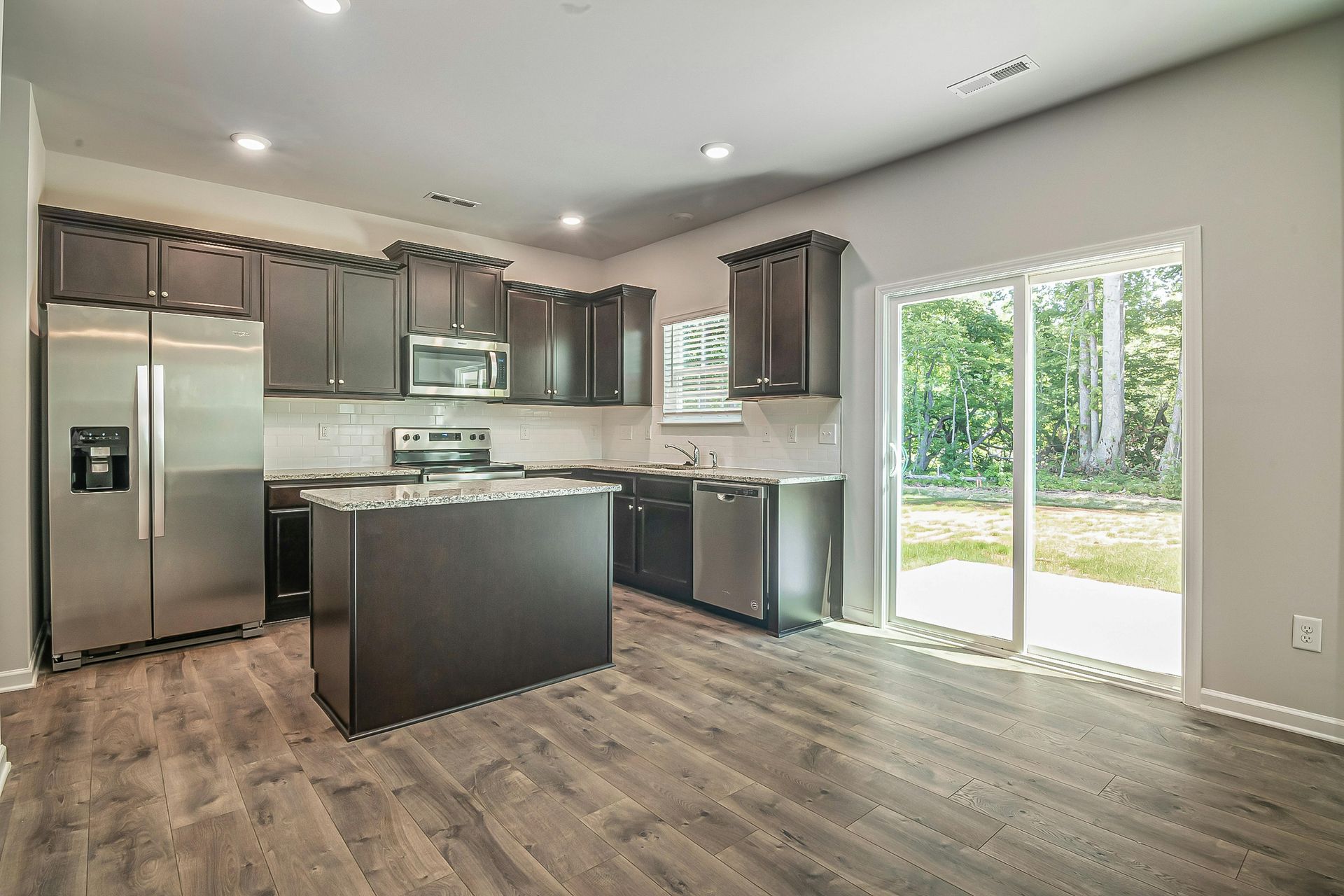 Modern kitchen with dark cabinetry, stainless steel appliances, island, and sliding glass door to backyard.