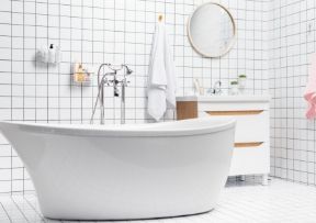 White bathroom with tub, vanity, and grid-tiled walls. A towel hangs, a mirror is on the wall.