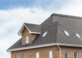 Brick house with dormer and skylights, dark roof, against a cloudy sky.