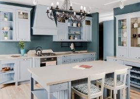 Blue kitchen with a central island, light cabinetry, and chandelier.