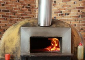 A brick pizza oven with flames burning inside, stainless steel front, and chimney.