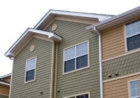 Two-story apartment building with green and tan siding, white trim, and multiple windows.