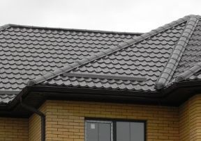 Grey metal roof on a brick building, with a dark gutter and a window visible.
