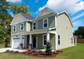 Two-story green house with white trim, porch, and a garage door, set on a green lawn with a blue sky.