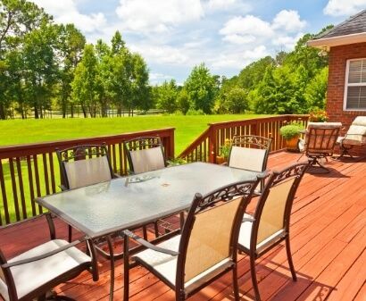 Wooden deck with table and chairs, overlooking a green lawn under a sunny sky.