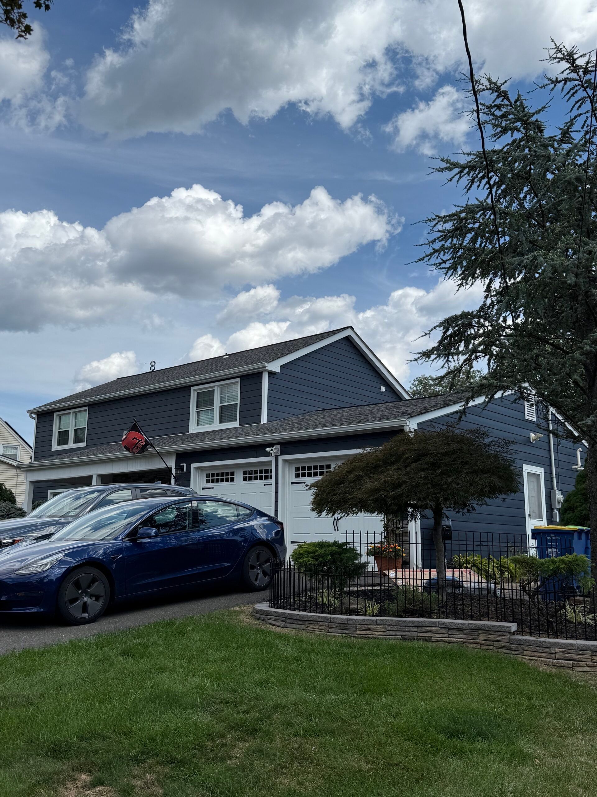 Blue house with white garage doors, blue car parked in the driveway, and a cloudy sky.