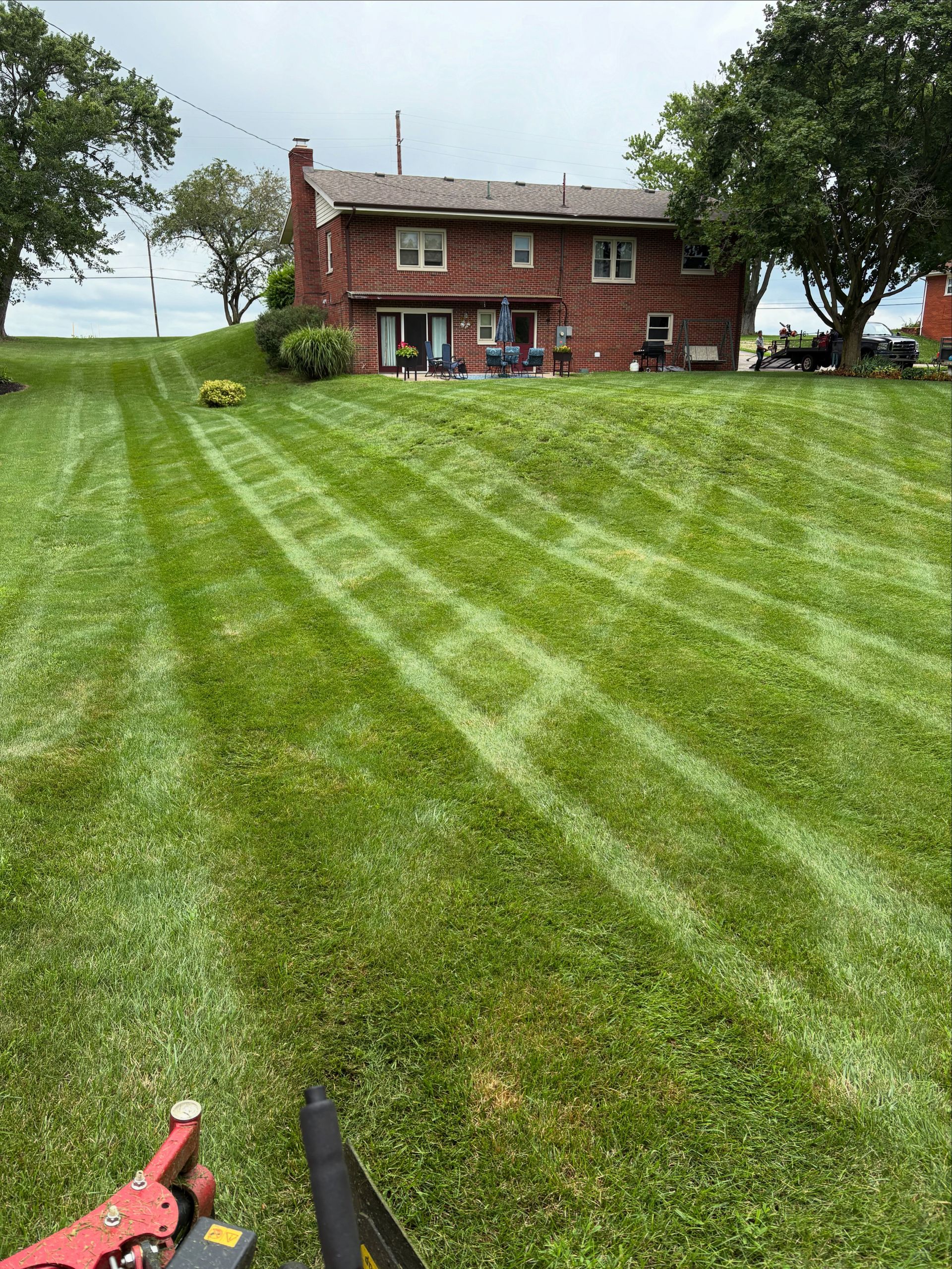 Lawn mowed with striped pattern up a grassy hill toward a brick house under a cloudy sky.