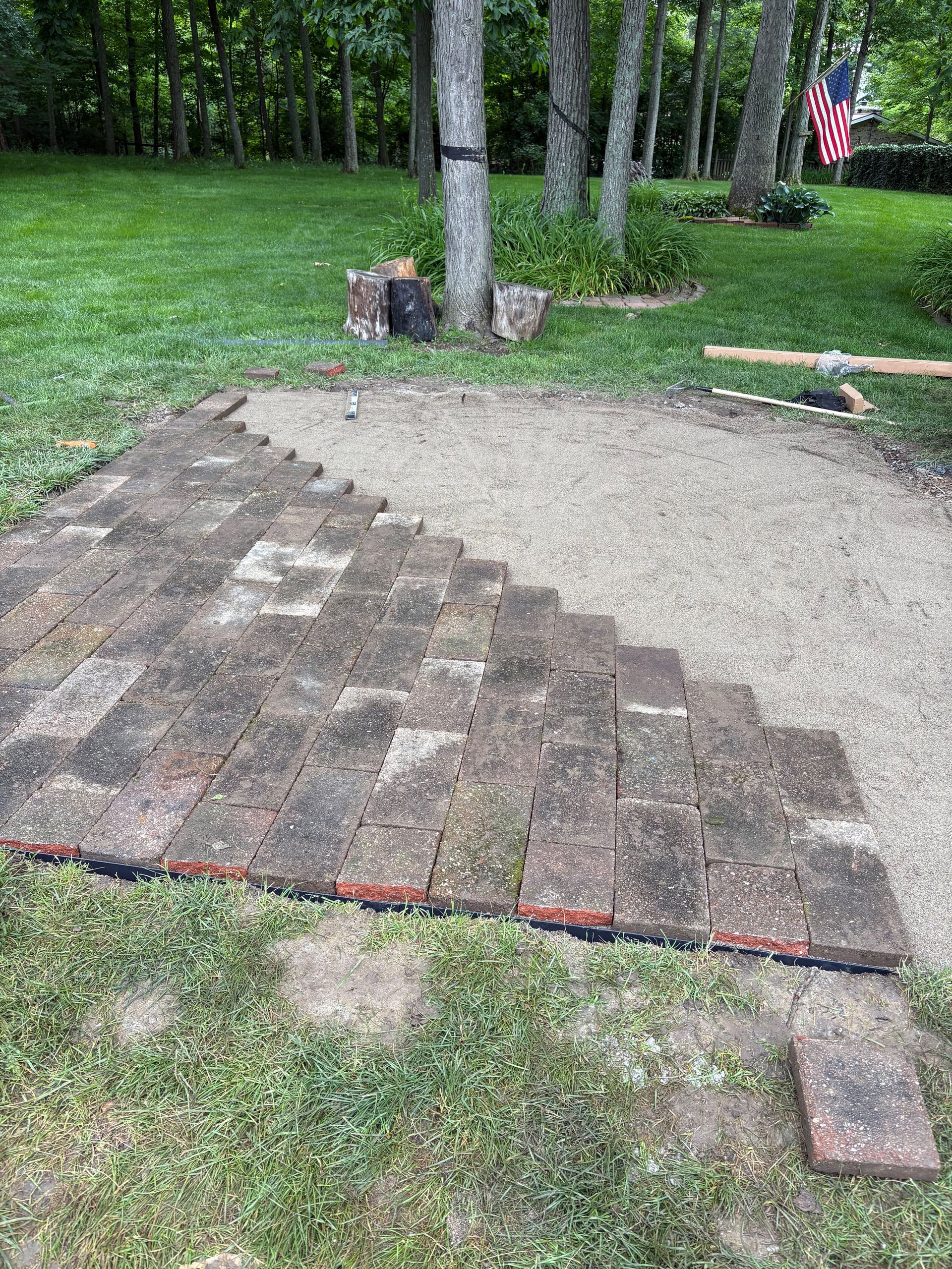 Bricks arranged in steps on gravel, in a yard. Trees and grass surround the patio.