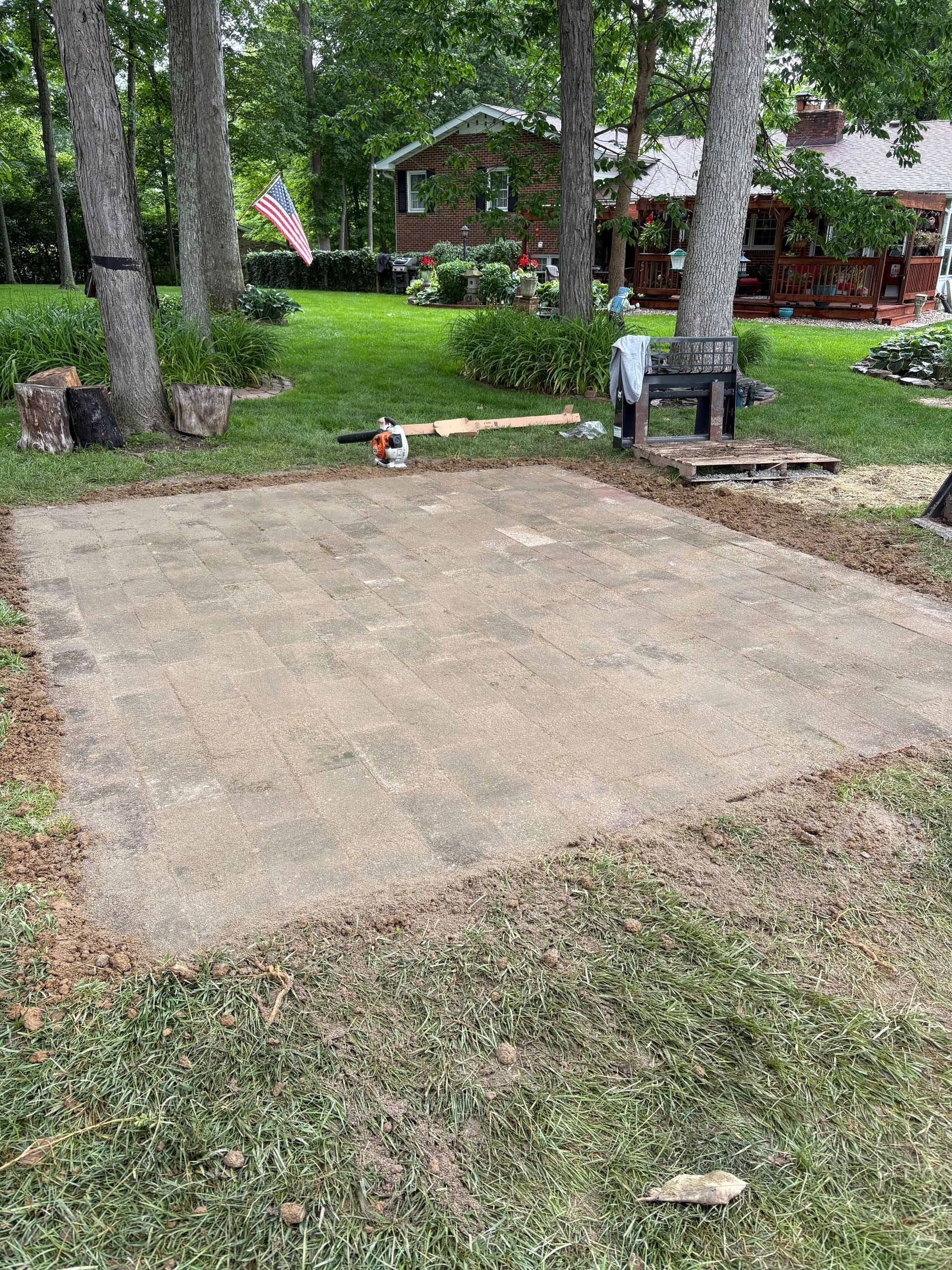 Cleared dirt patio area with grassy edges in a backyard setting.
