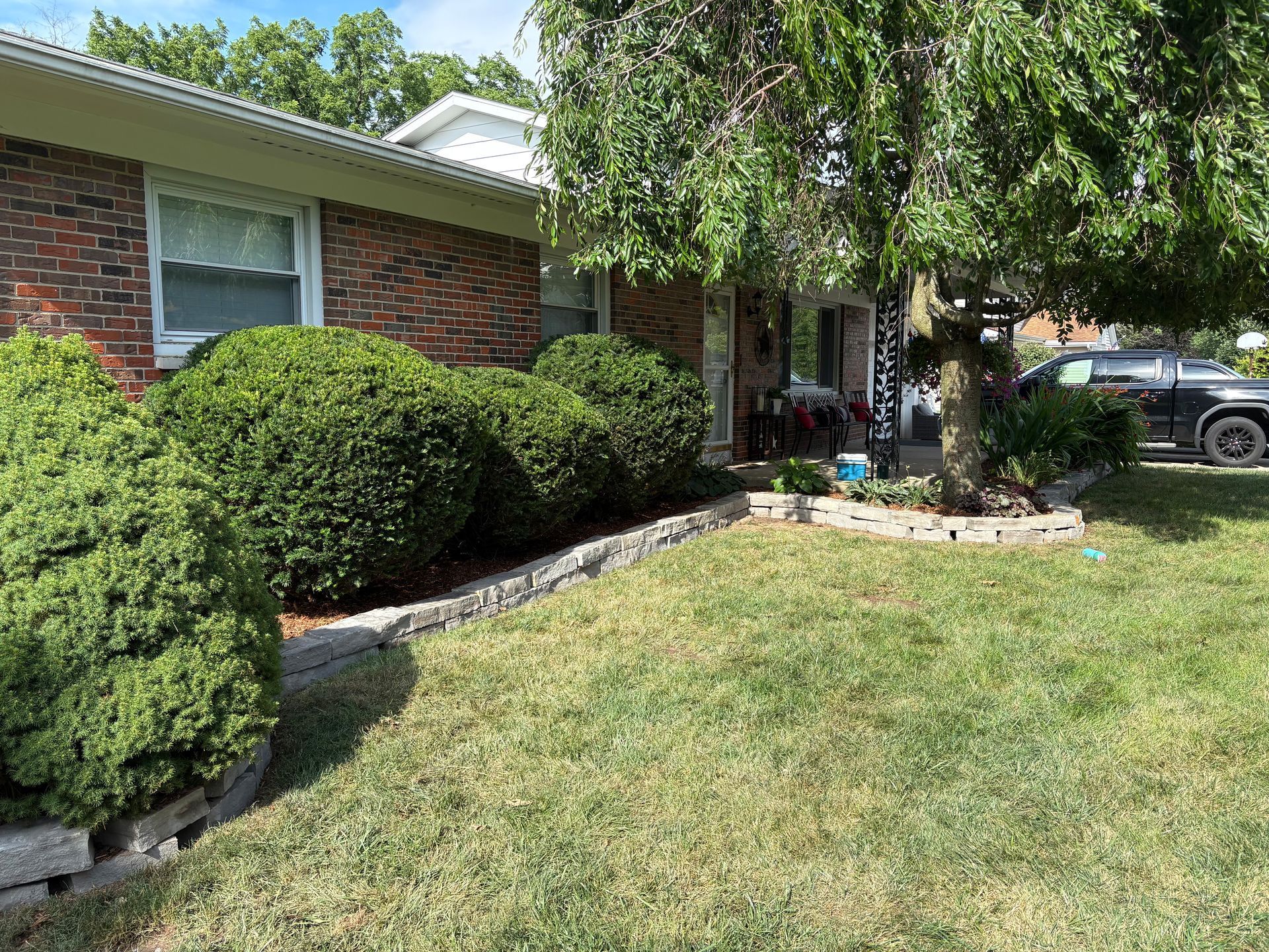 Brick house with manicured bushes, a tree, and a lawn. Black truck parked in the driveway.