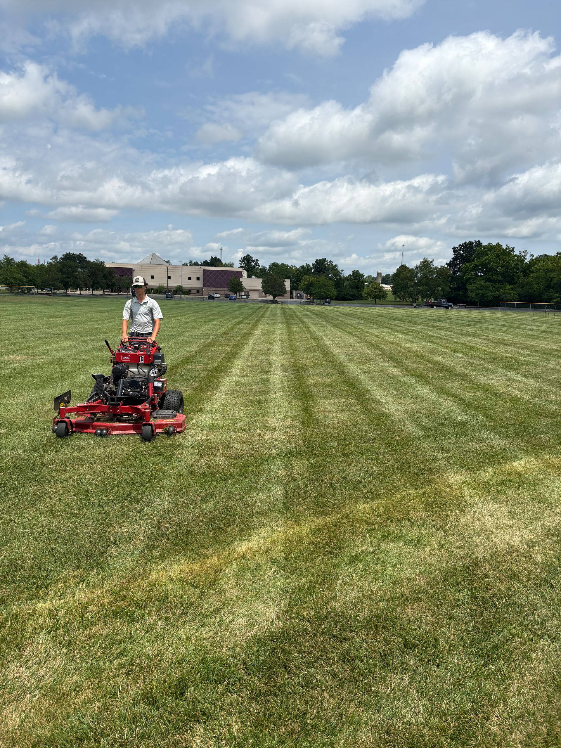 Man mowing a large lawn with a red riding mower on a sunny day.