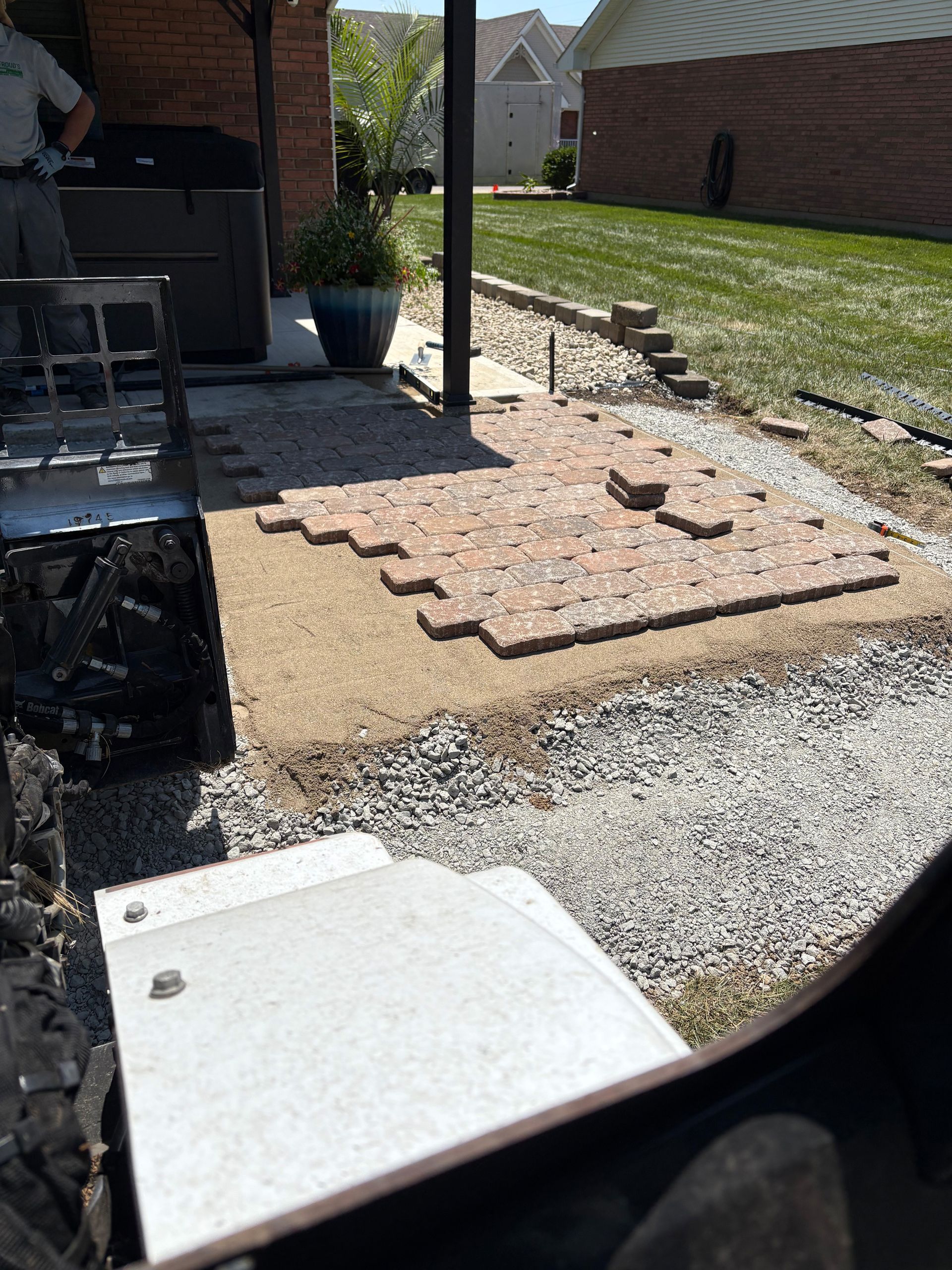 Patio construction with brick pavers, gravel base, and person standing nearby.