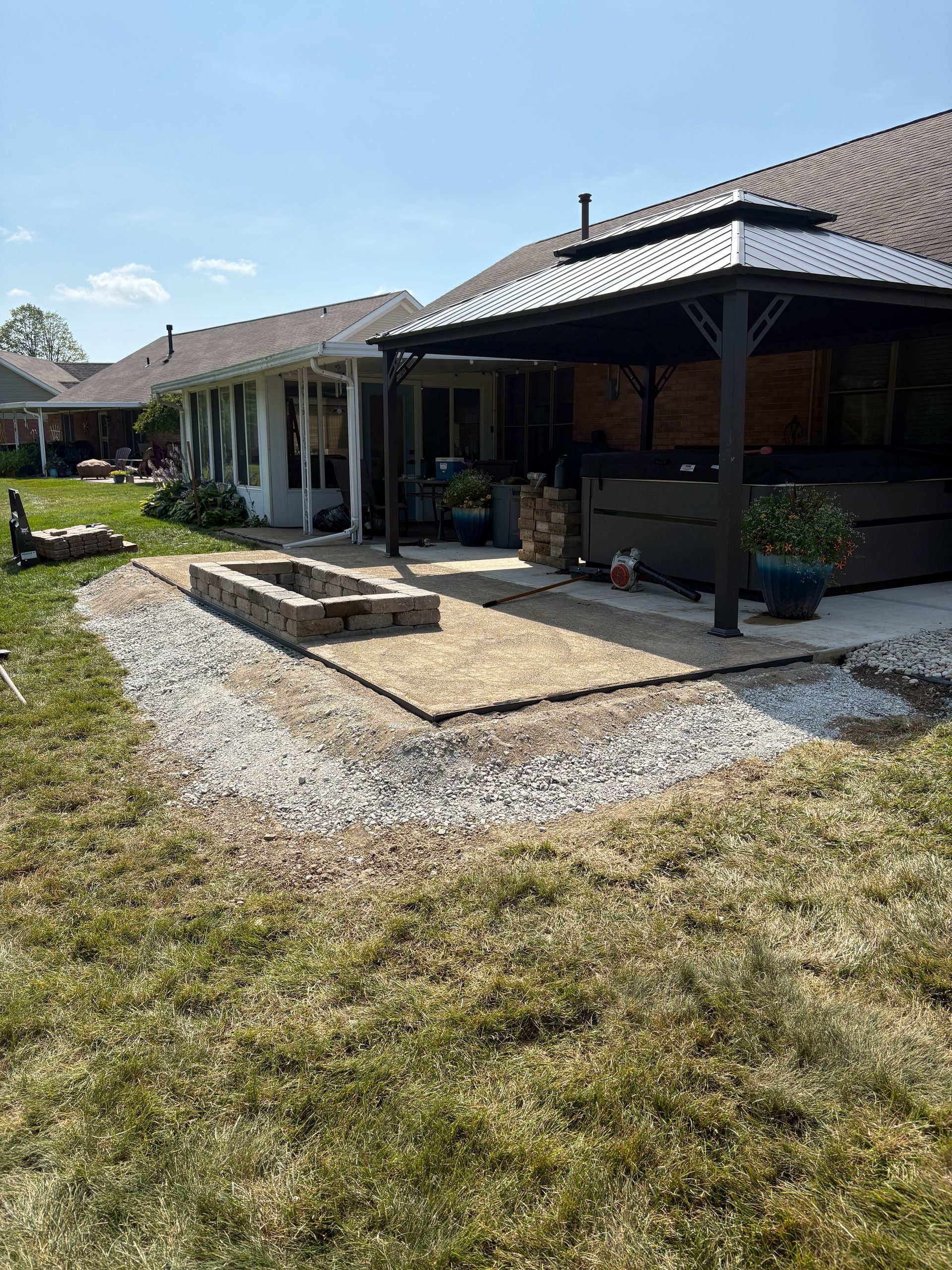 Backyard patio with a fire pit and gazebo near a house on a sunny day.