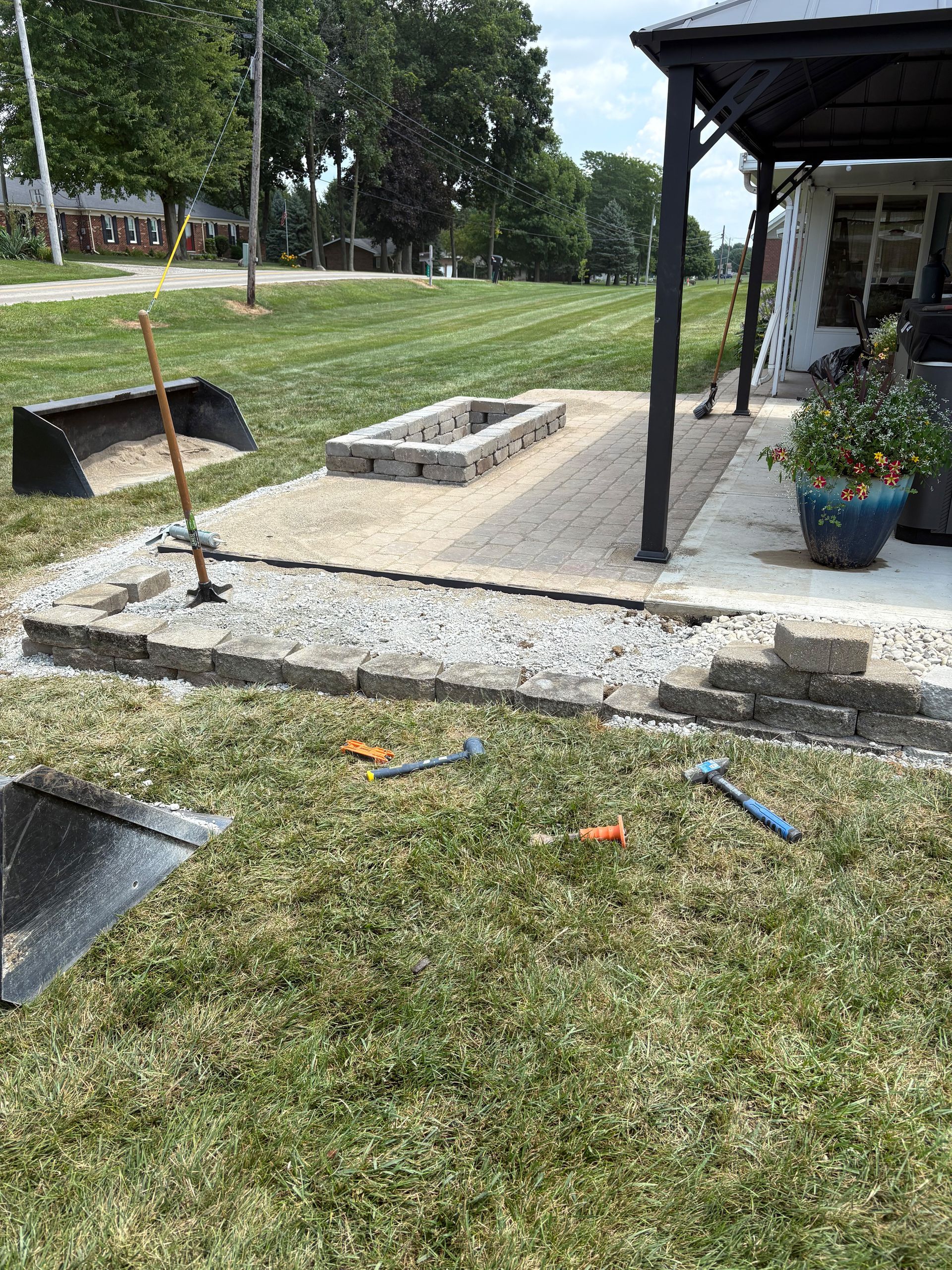 Backyard patio under construction with gravel, pavers, and a fire pit.
