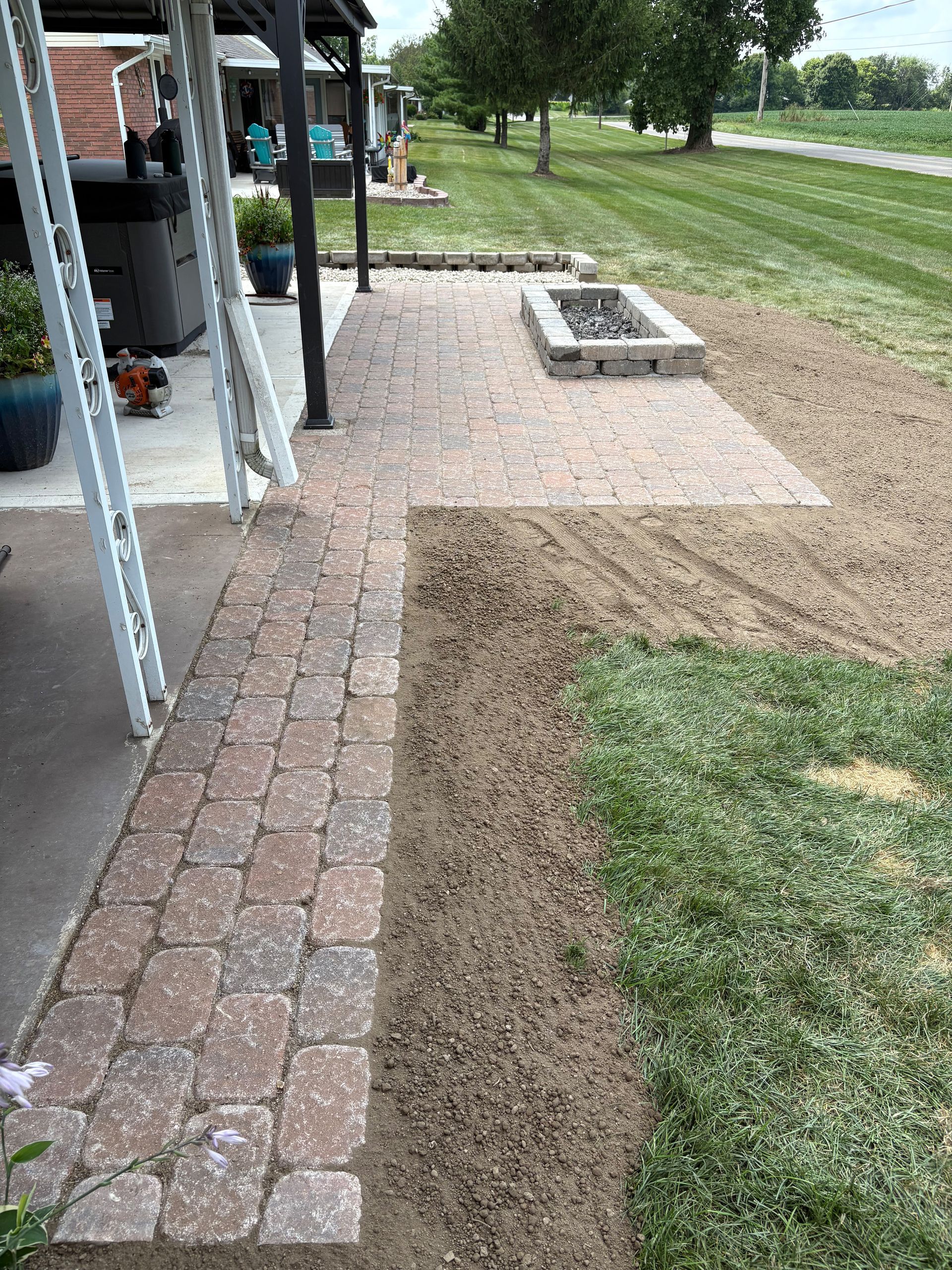 Brick patio extending to gravel and grassy areas with a fire pit.