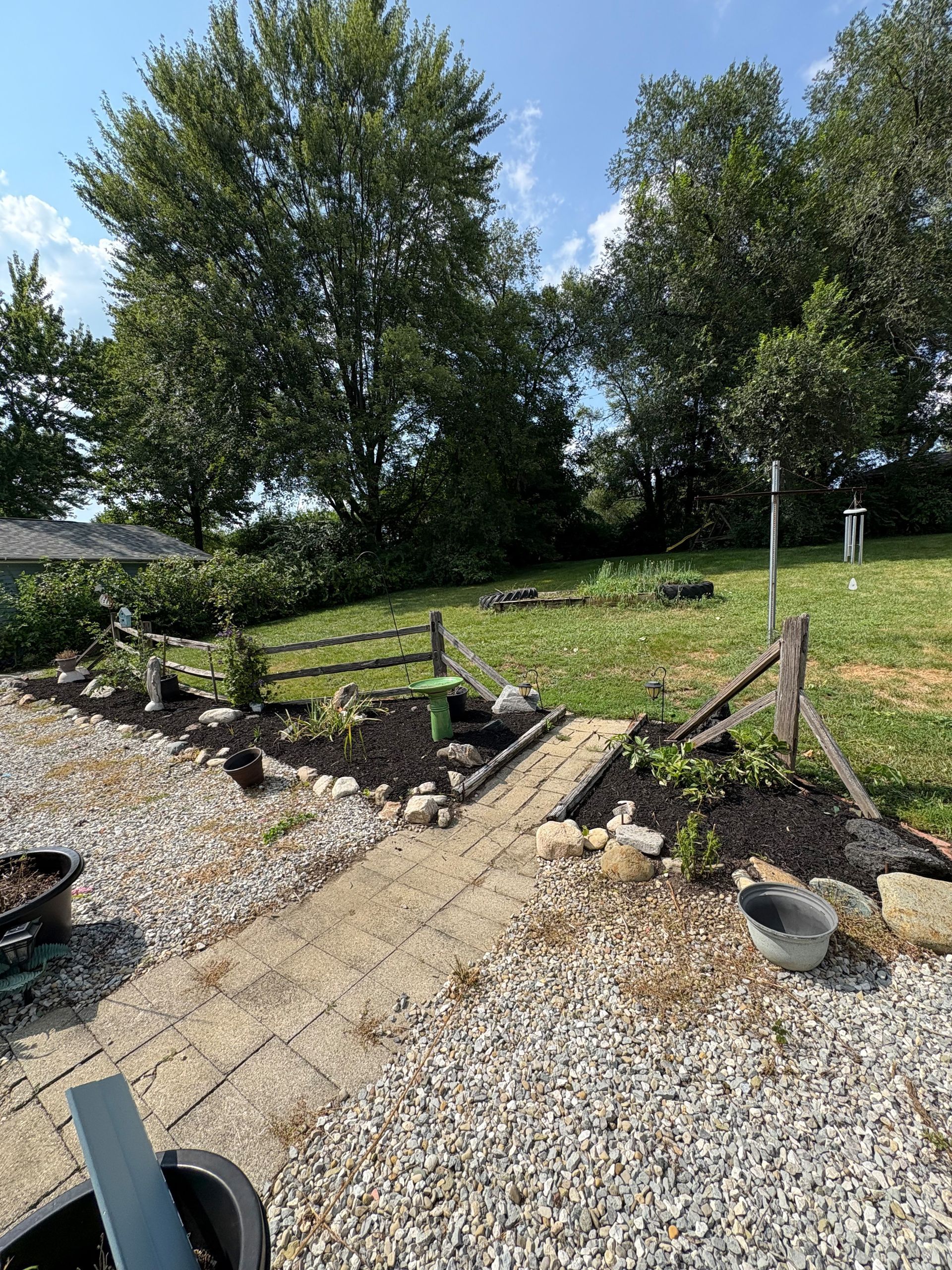 A stone path leads to a garden with a wooden fence and green grass, under a blue sky.