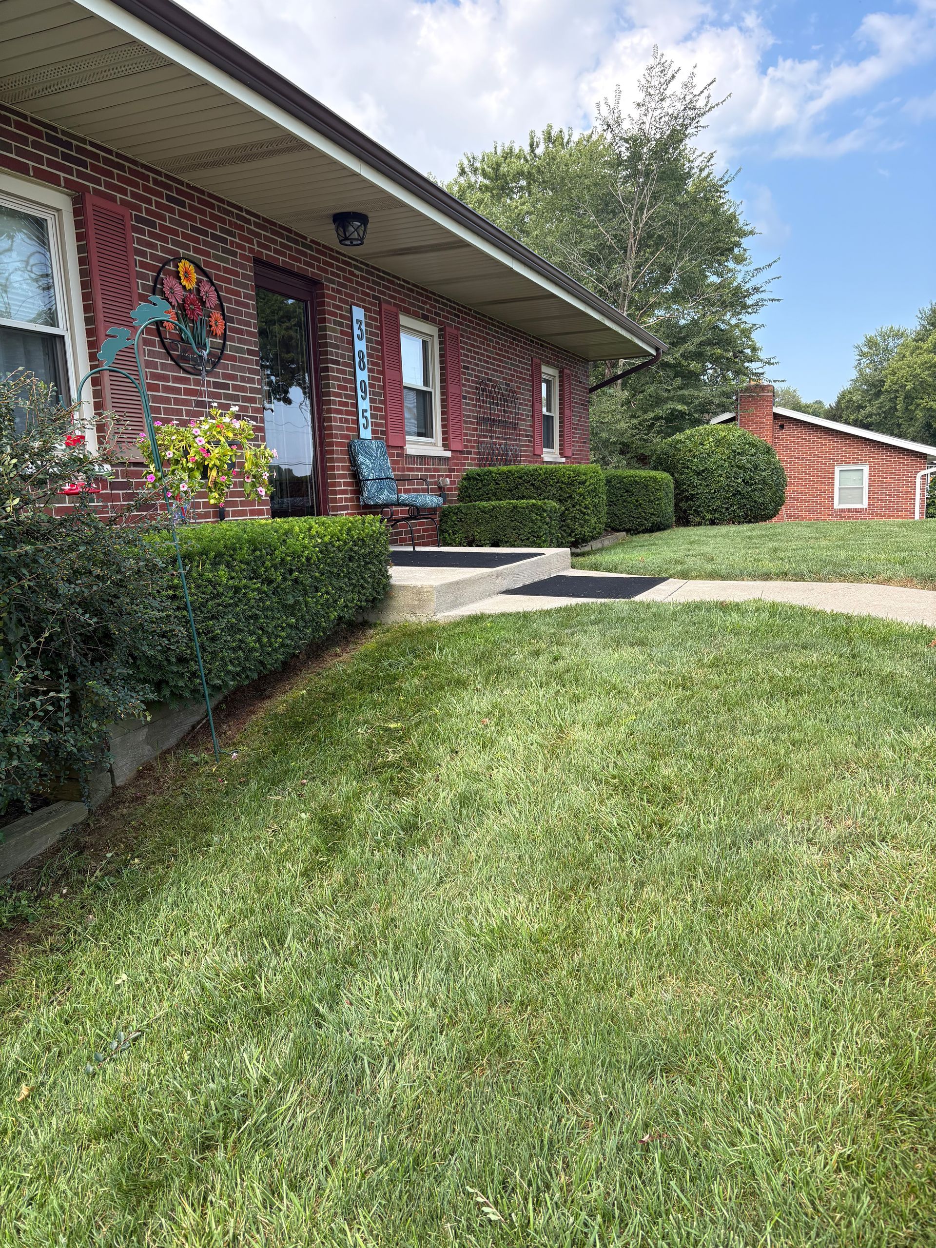 Red brick house with green bushes, lawn, and blue sky.