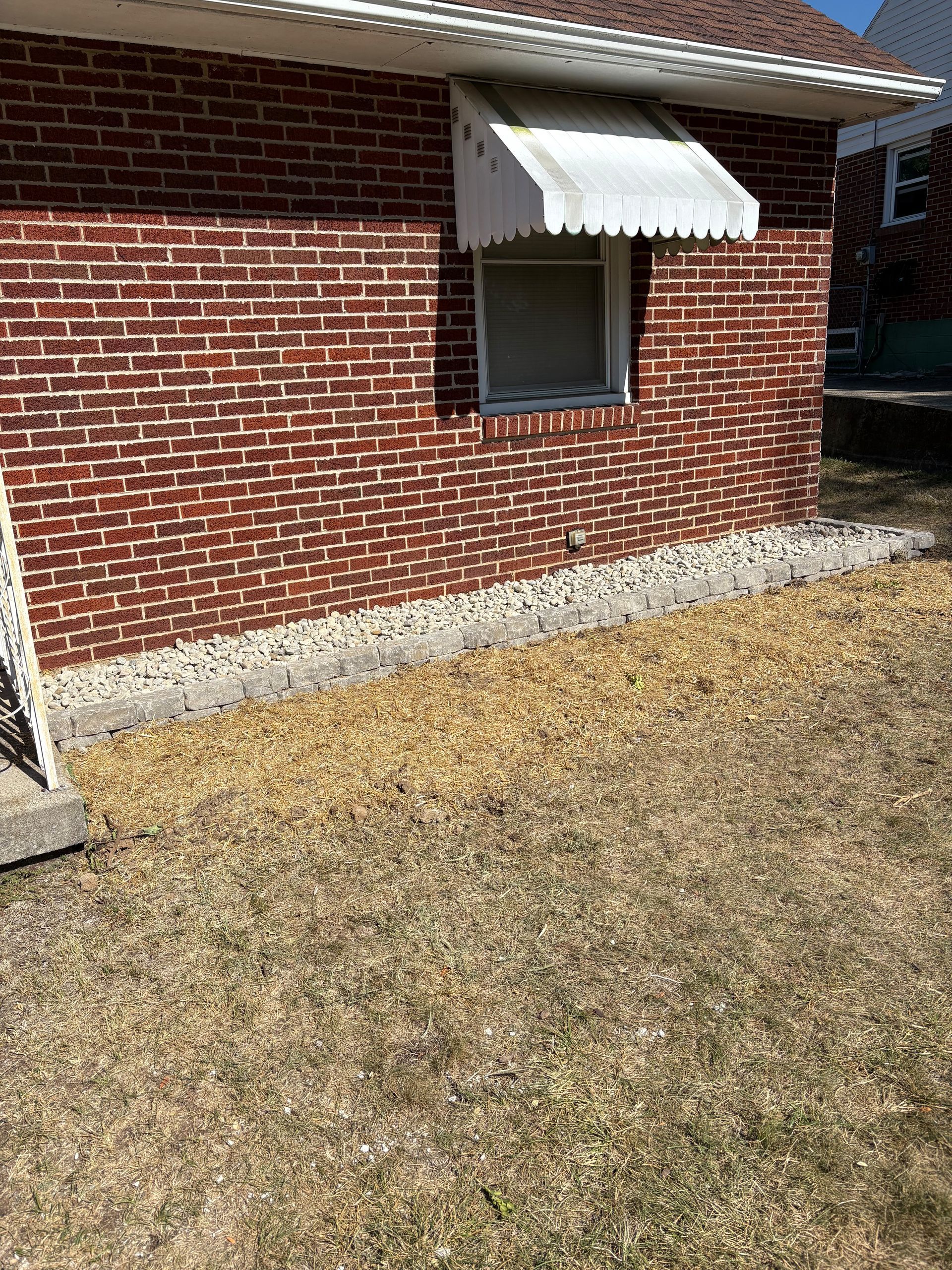 Red brick building with an awning over a window, brown dried grass in the foreground.