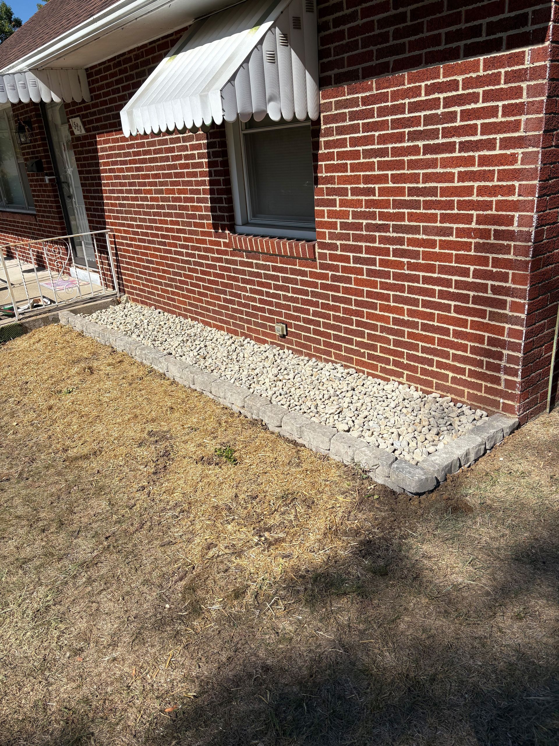 Brick house exterior with a low concrete border, dry grass.