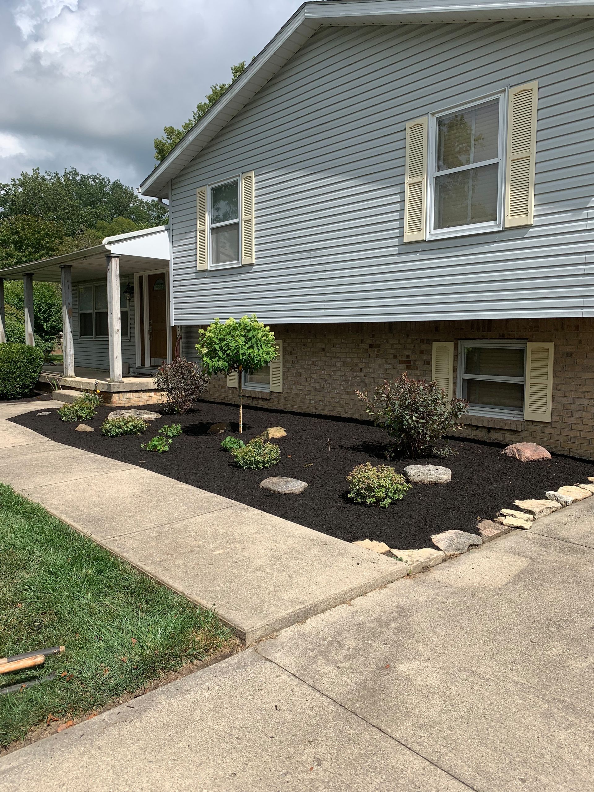 House with fresh black mulch in front flowerbeds, green grass, and a concrete walkway.