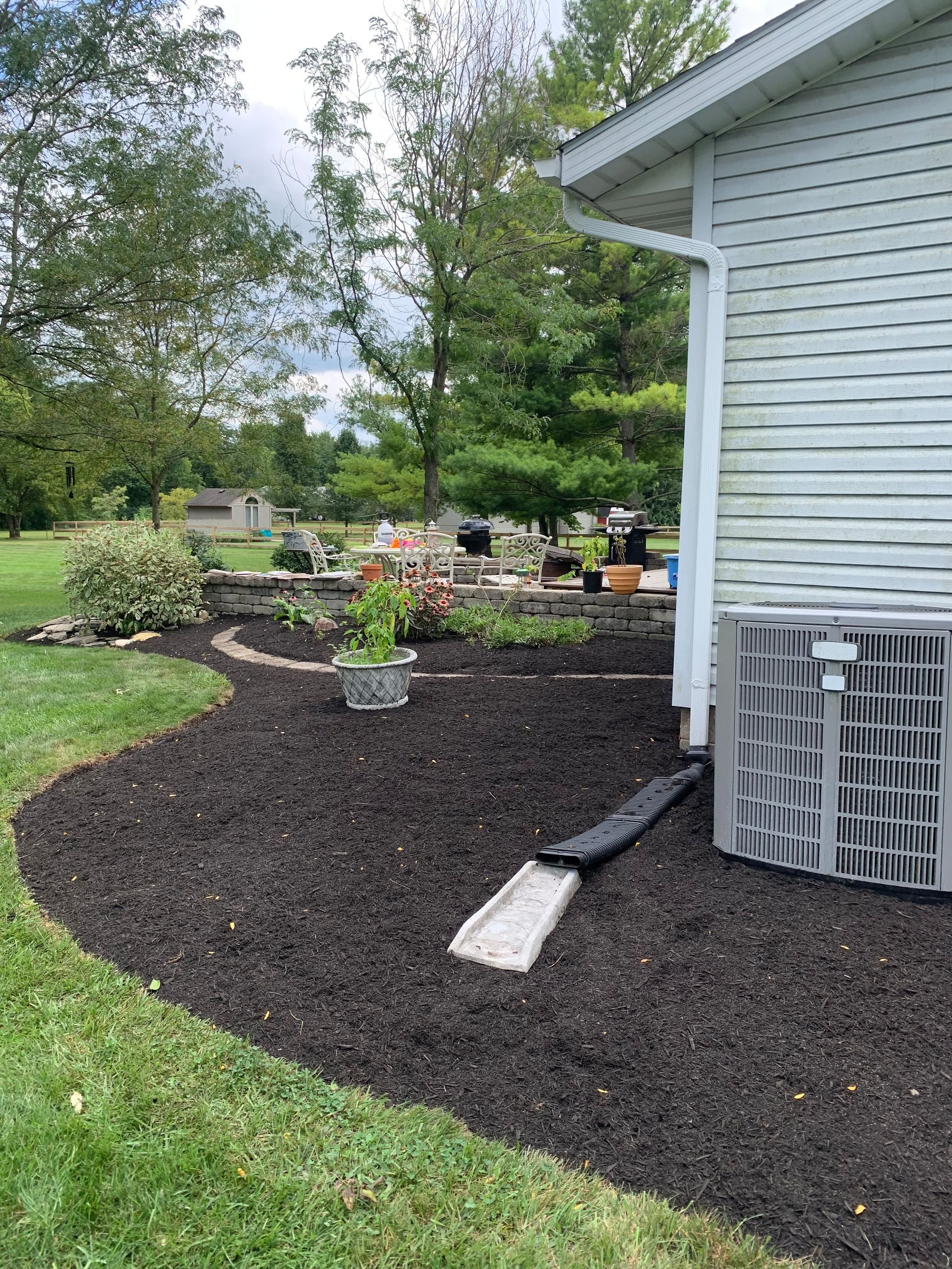 A backyard with a garden bed with fresh mulch, a house, and an AC unit.