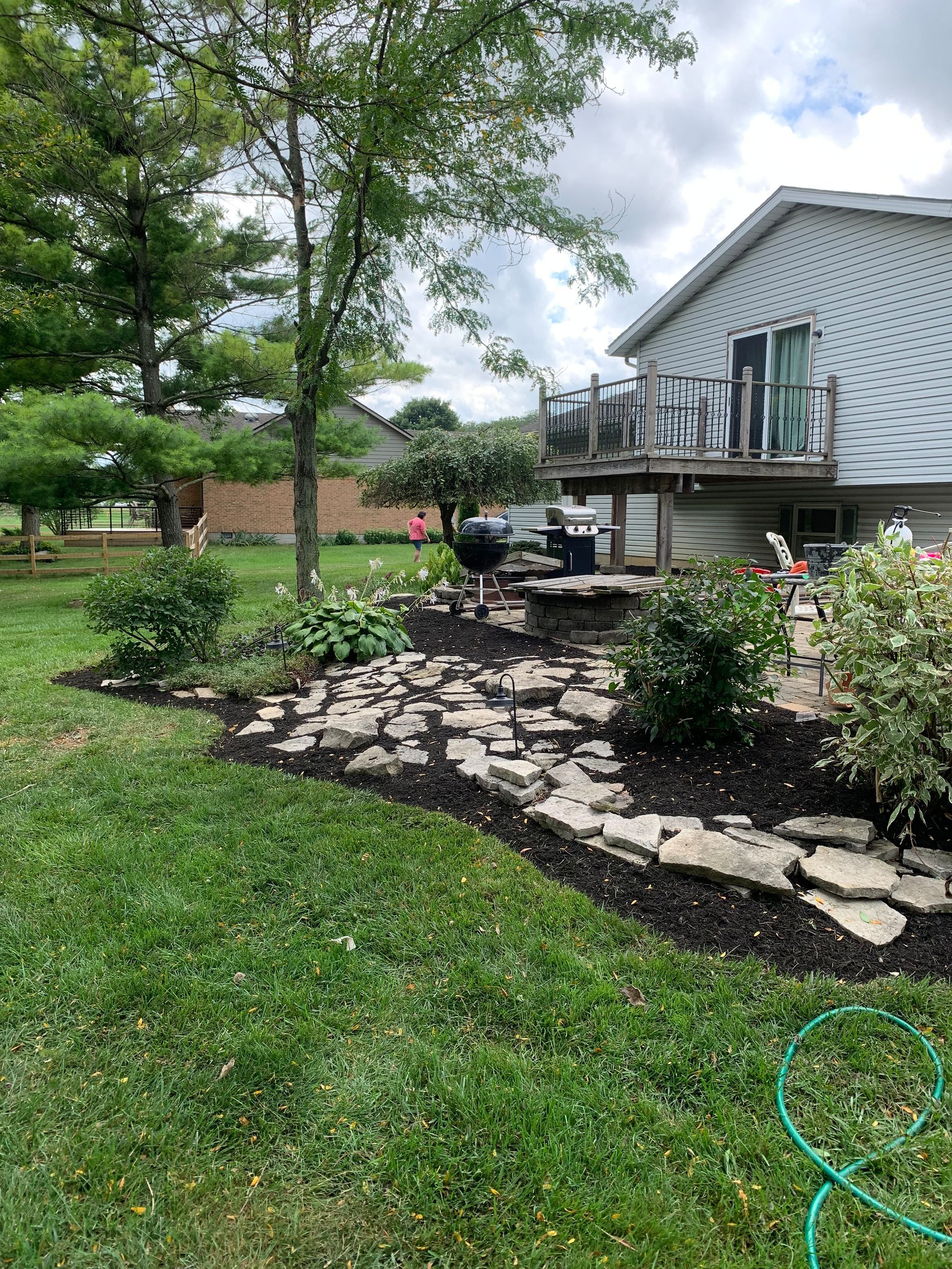 Backyard garden bed with rocks and plants next to a house with a deck, mulched bed with bushes.