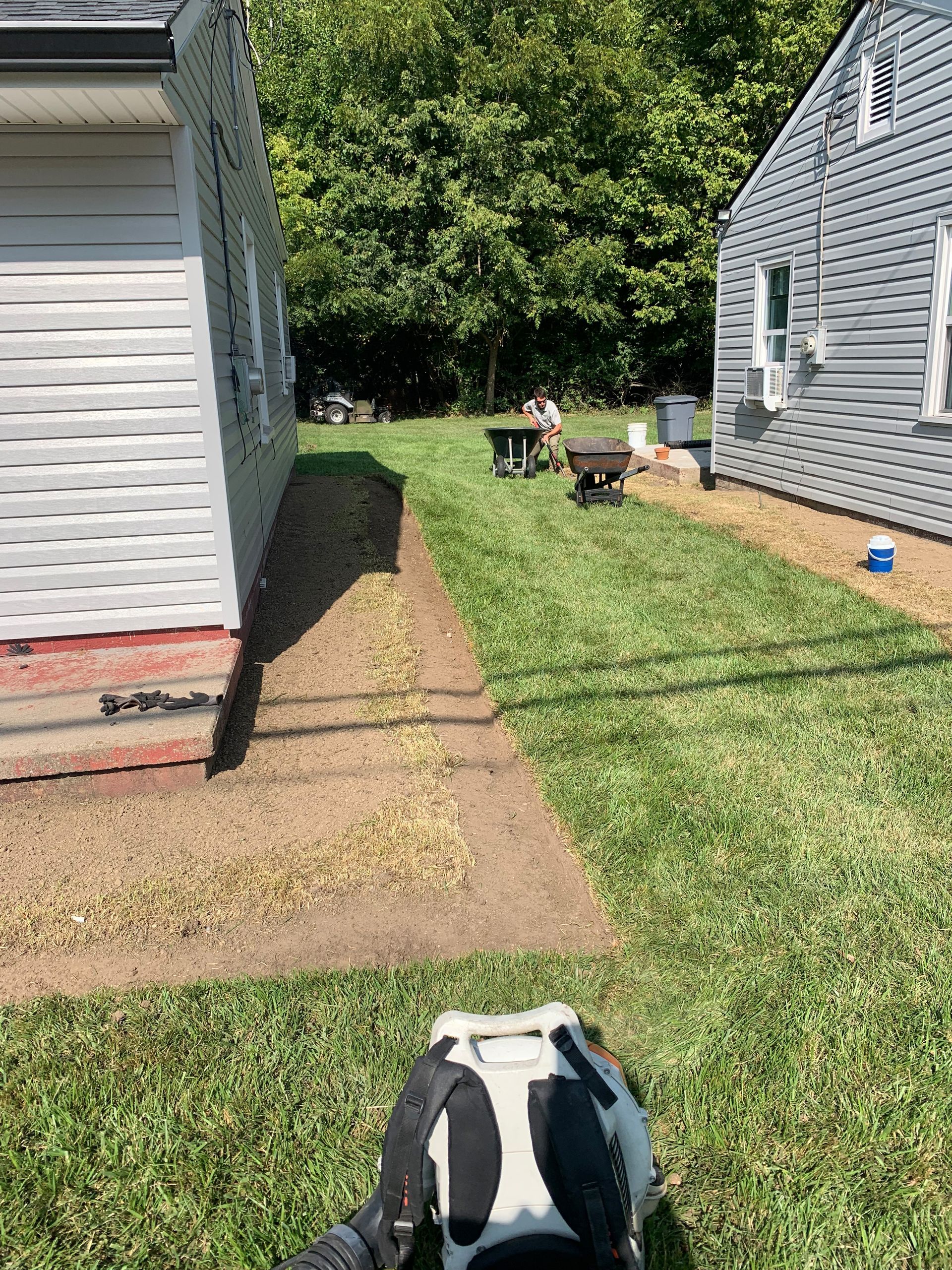Workers spreading gravel between two houses, sunny day.