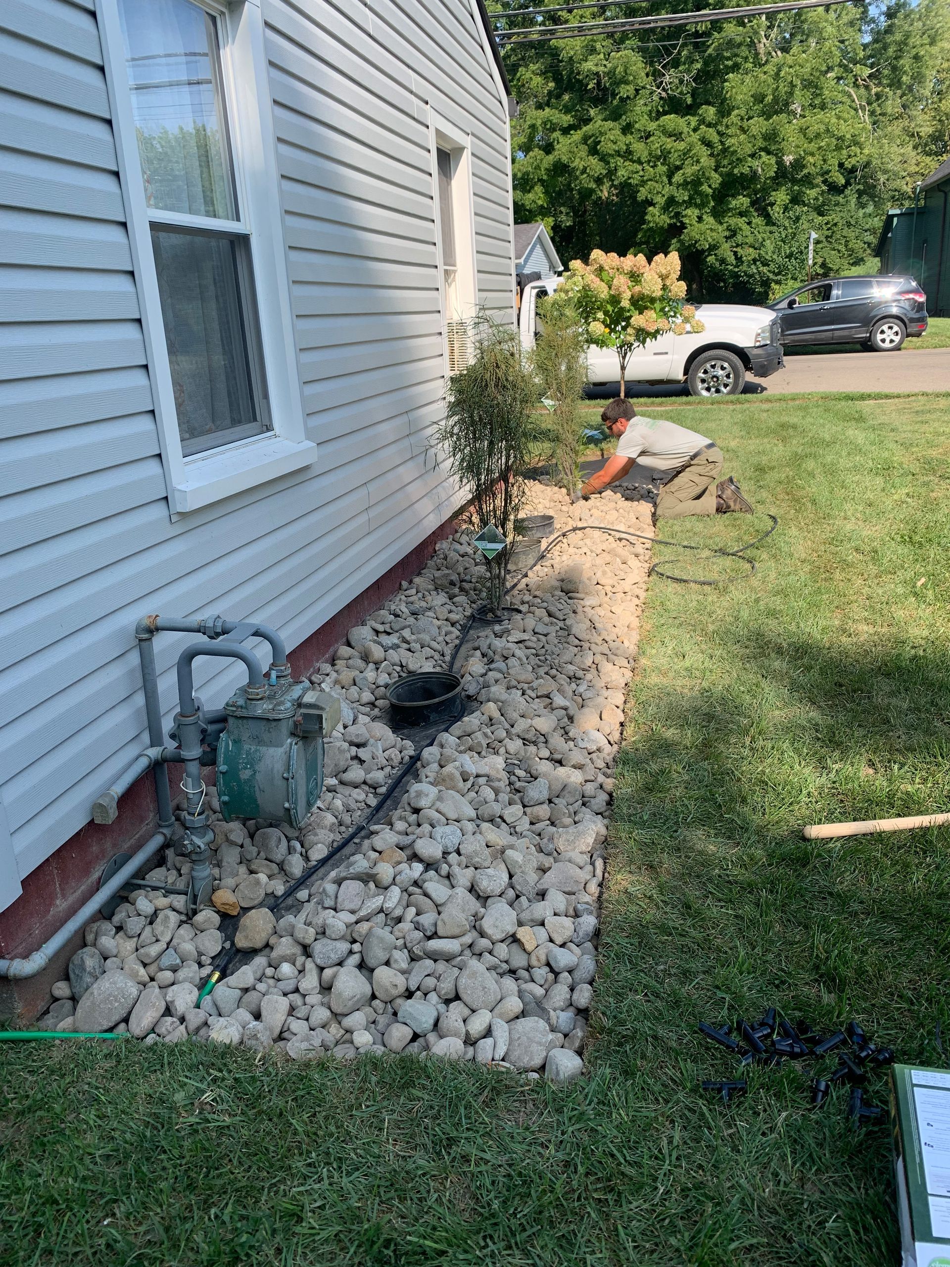 Side of a house with rock landscaping, gas meter, and small plants against light siding.