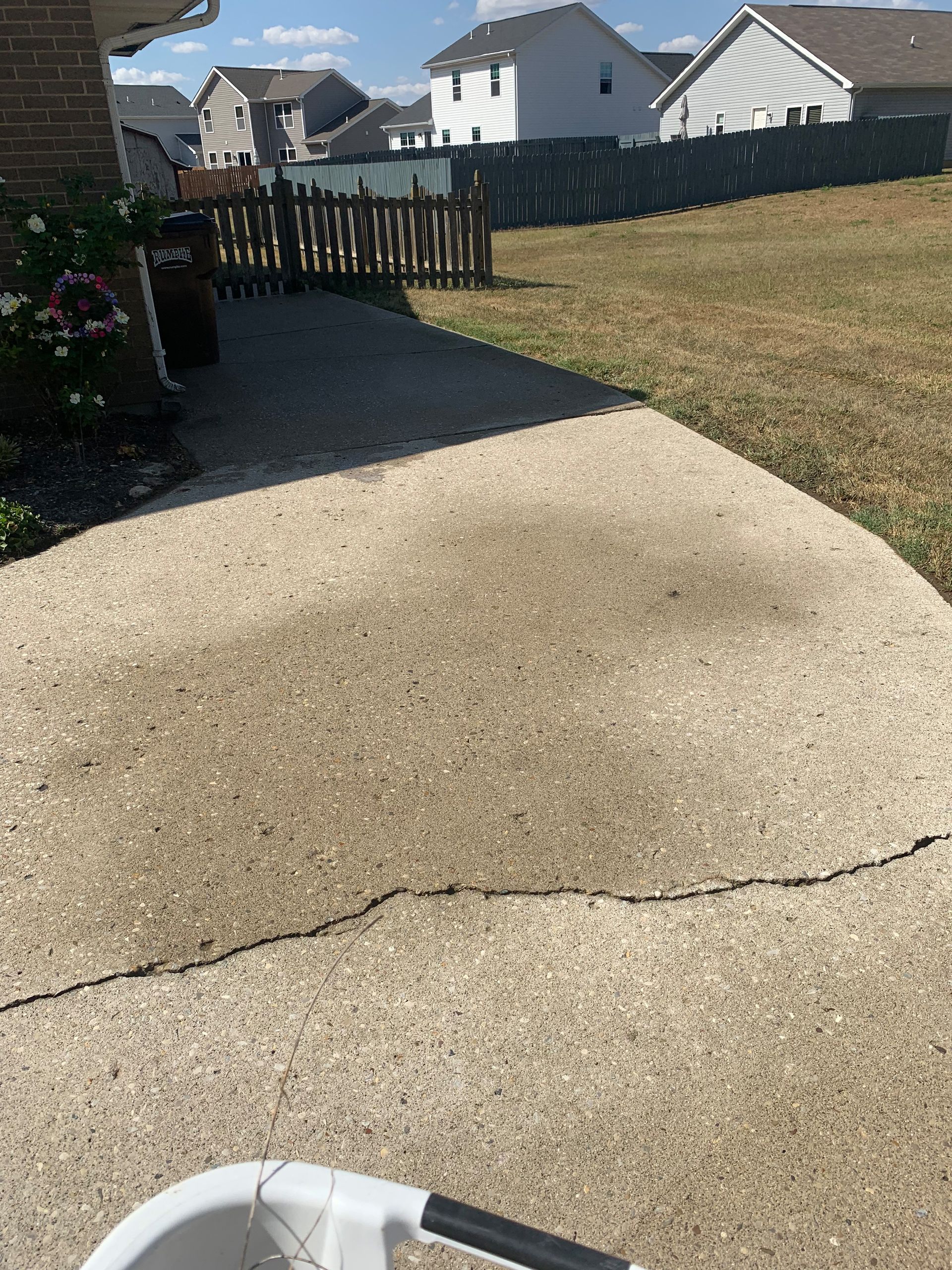 Concrete patio with a long crack, leading to a backyard with brown grass and a fence.