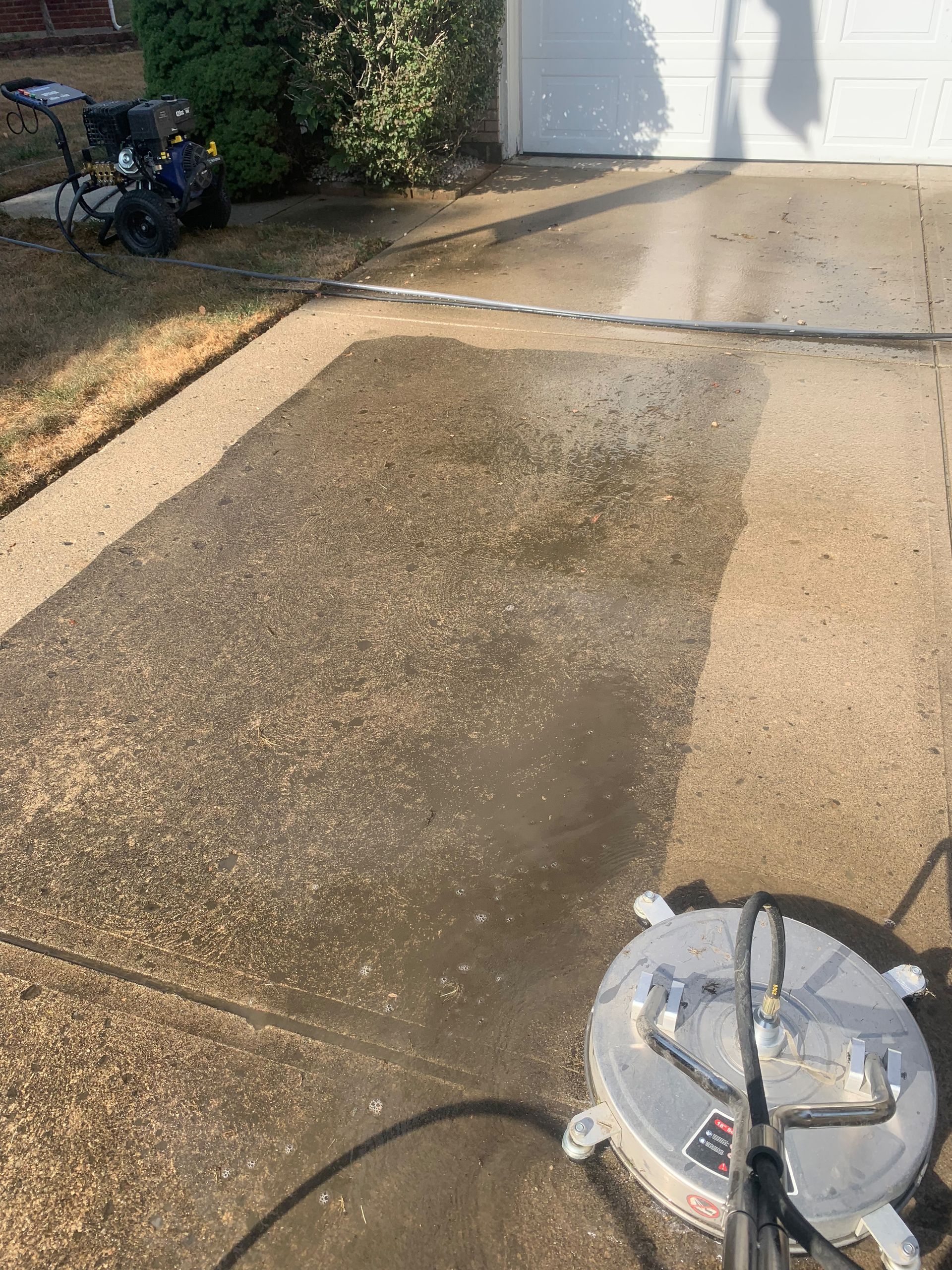 Power washing a concrete driveway with a circular surface cleaner.