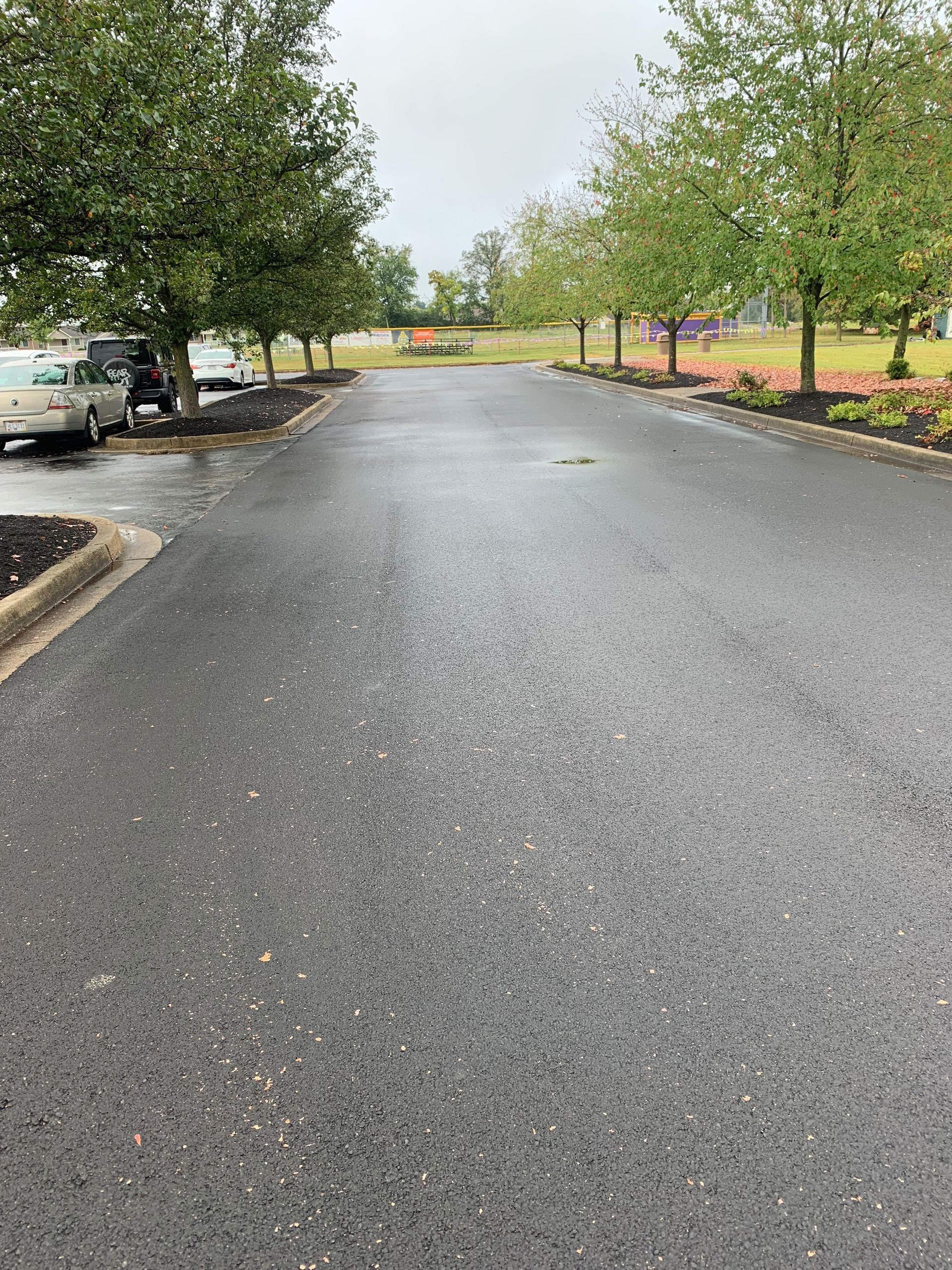 Wet asphalt road lined with trees and landscaping. Overcast sky.