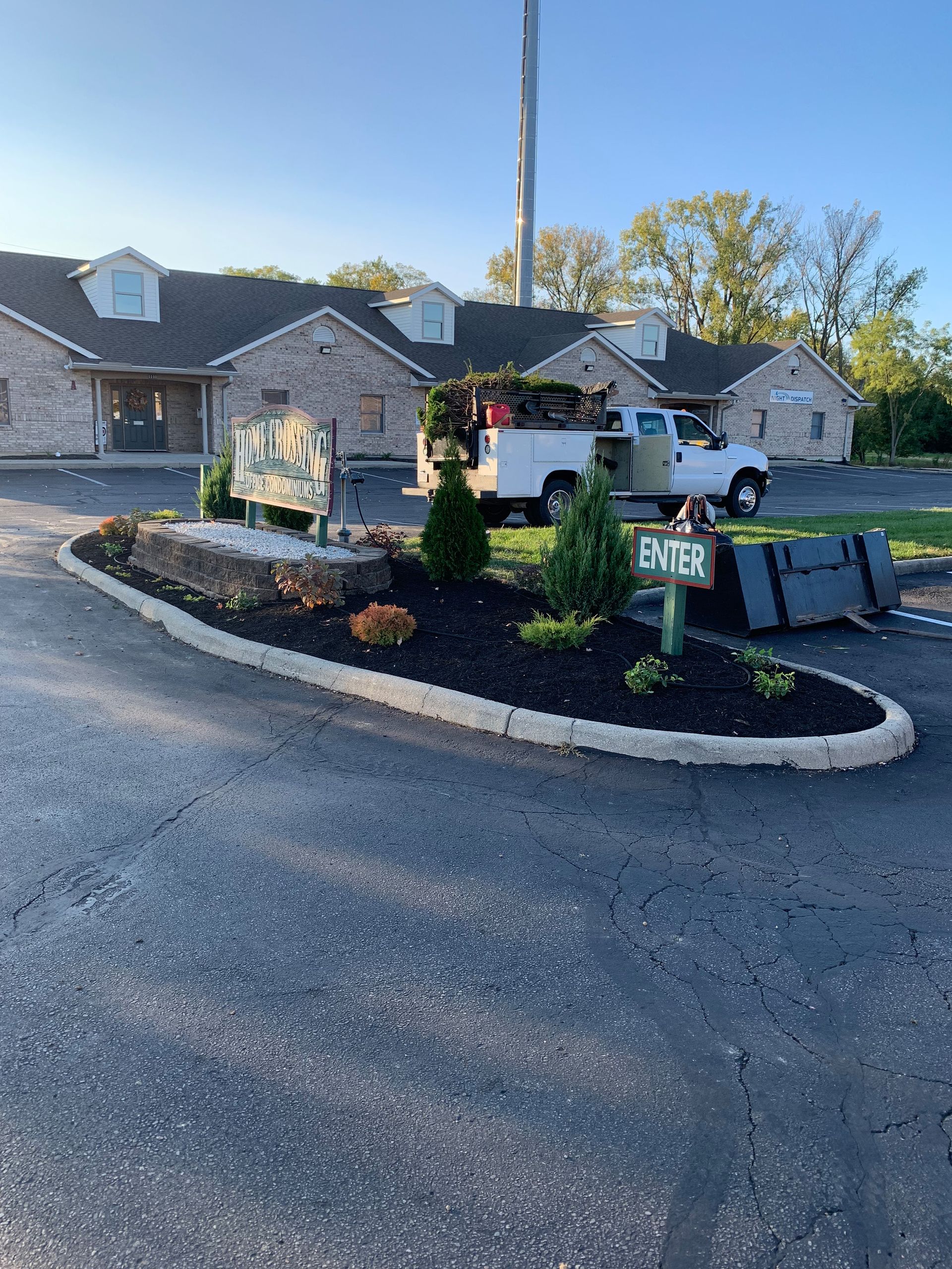 A light-colored brick building with a small landscaping area and work truck; 