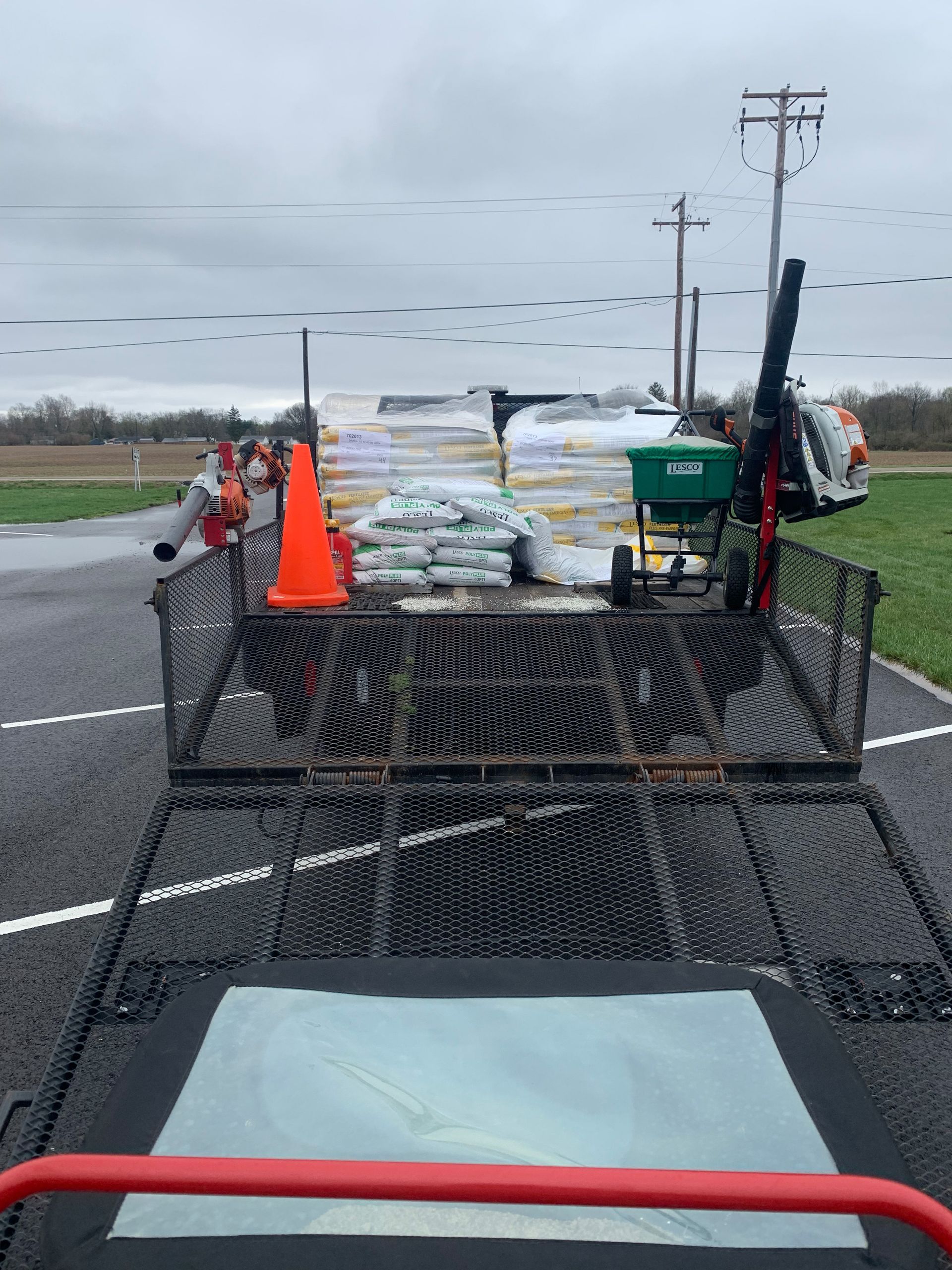 Trailer loaded with bags, spreader, and cone parked on asphalt.