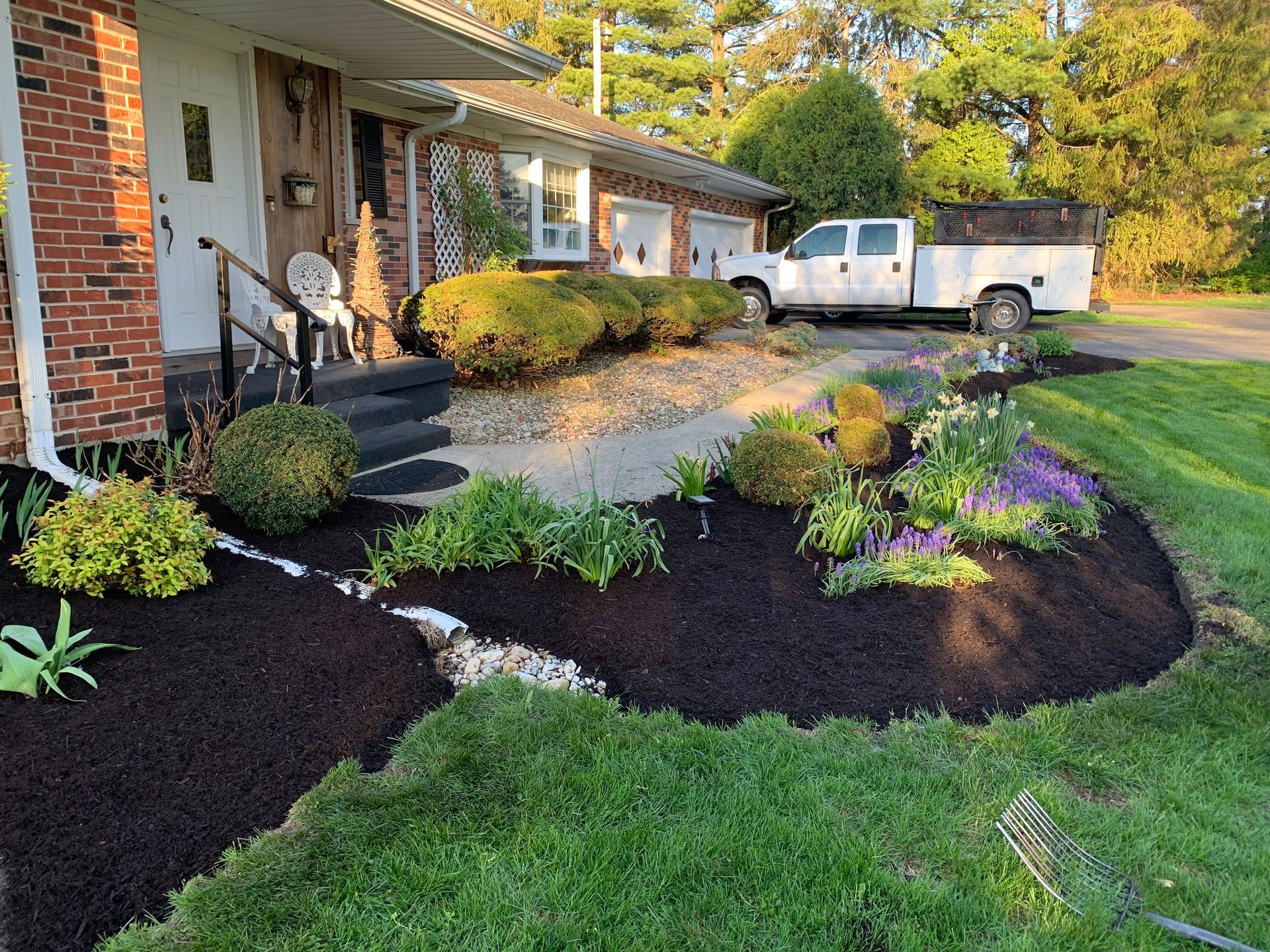 A well-manicured front yard with fresh mulch, a brick house, and a white pickup truck parked nearby.