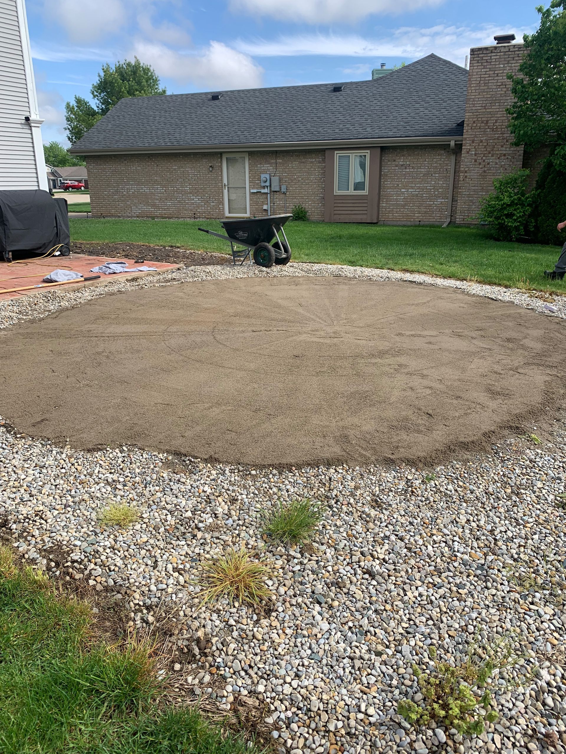 A gravel patio under construction, surrounded by landscaping rocks, in a backyard setting.