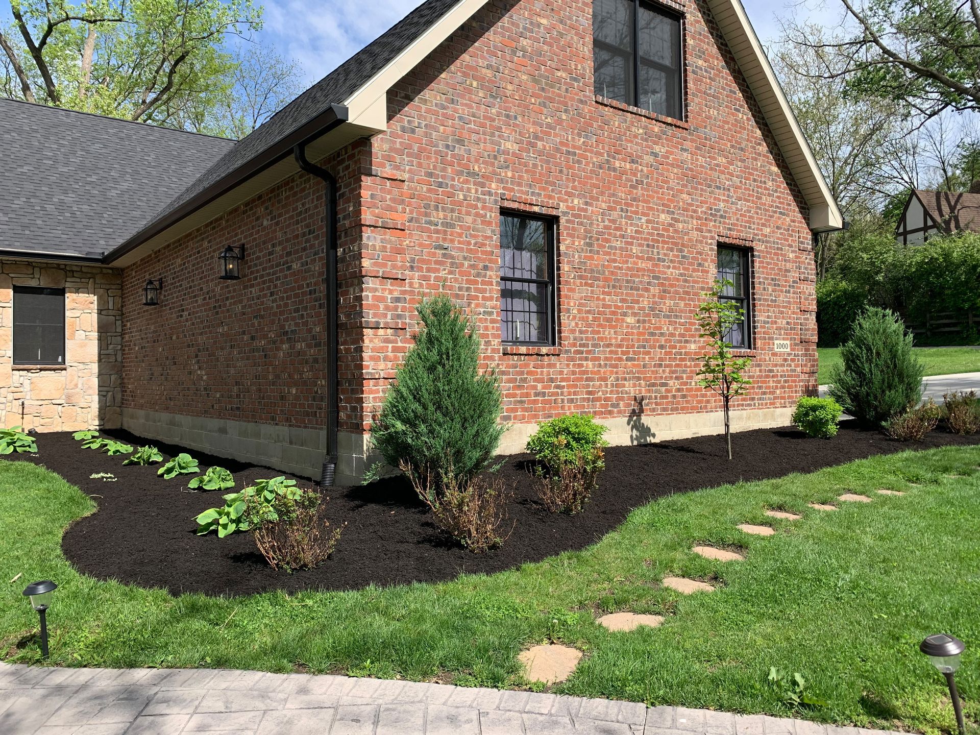 Brick house with a garden bed of dark mulch and stepping stones in the yard.