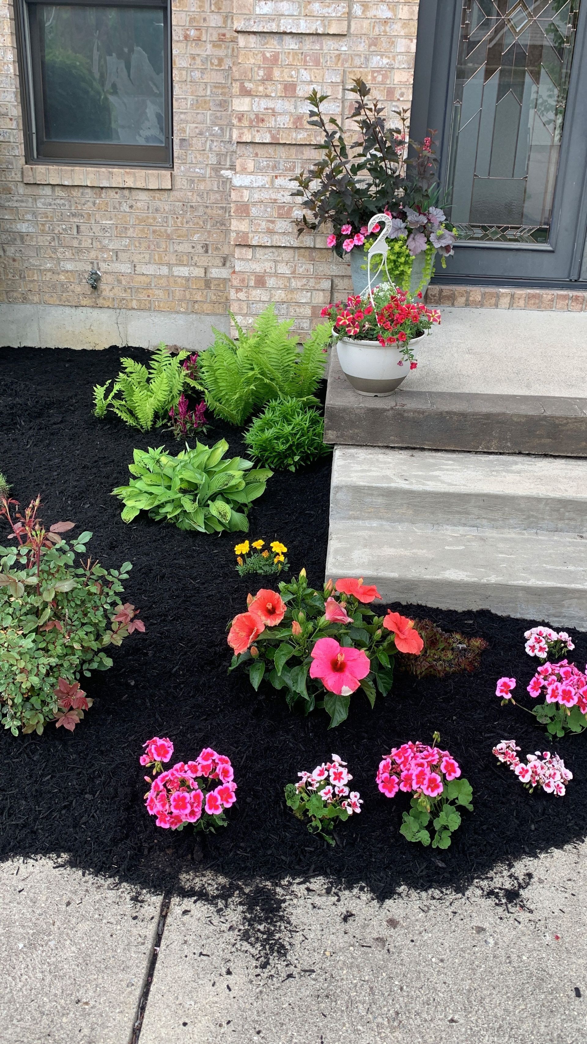 Flower bed with pink and red flowers in front of a brick building.
