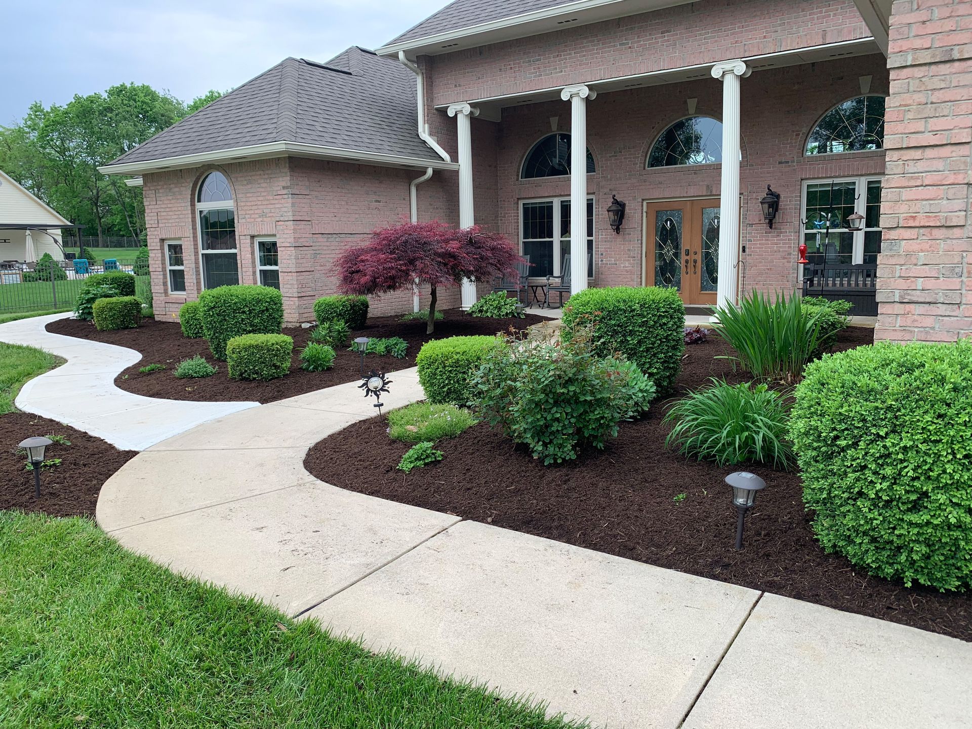 Brick home with a winding sidewalk lined with green shrubs and dark mulch.