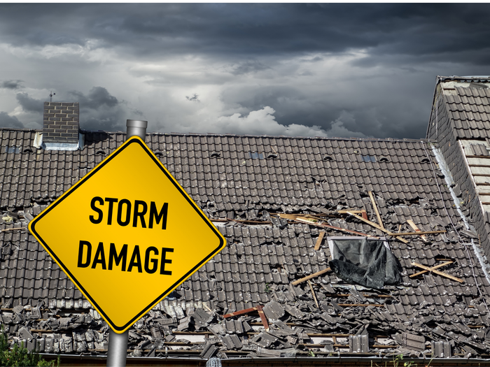 Severely damaged roof under dark storm clouds with a warning sign, emphasizing the importance of a home and auto insurance broker service in Maricopa, AZ