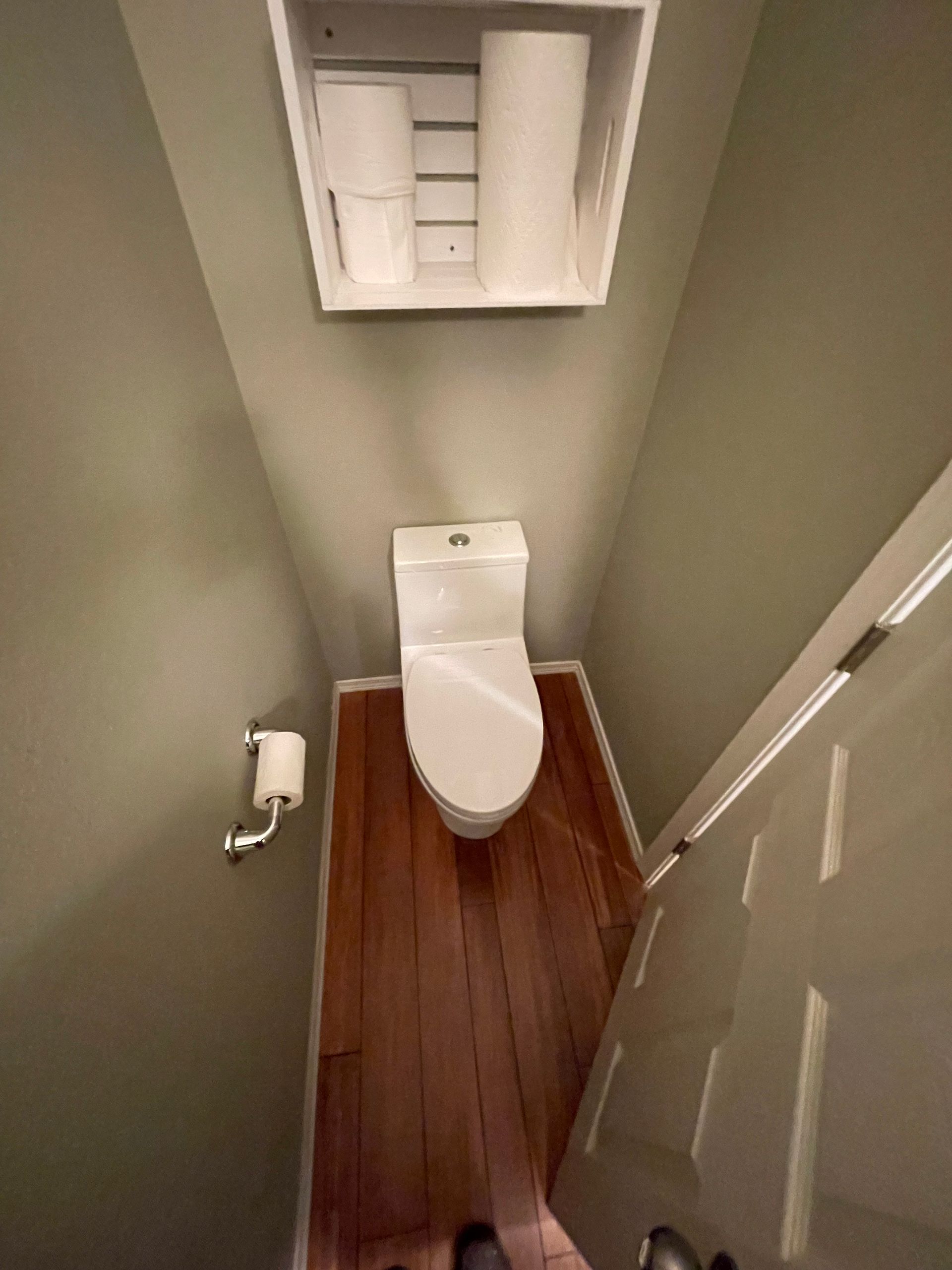 A small bathroom with a toilet and a shelf with toilet paper on it.