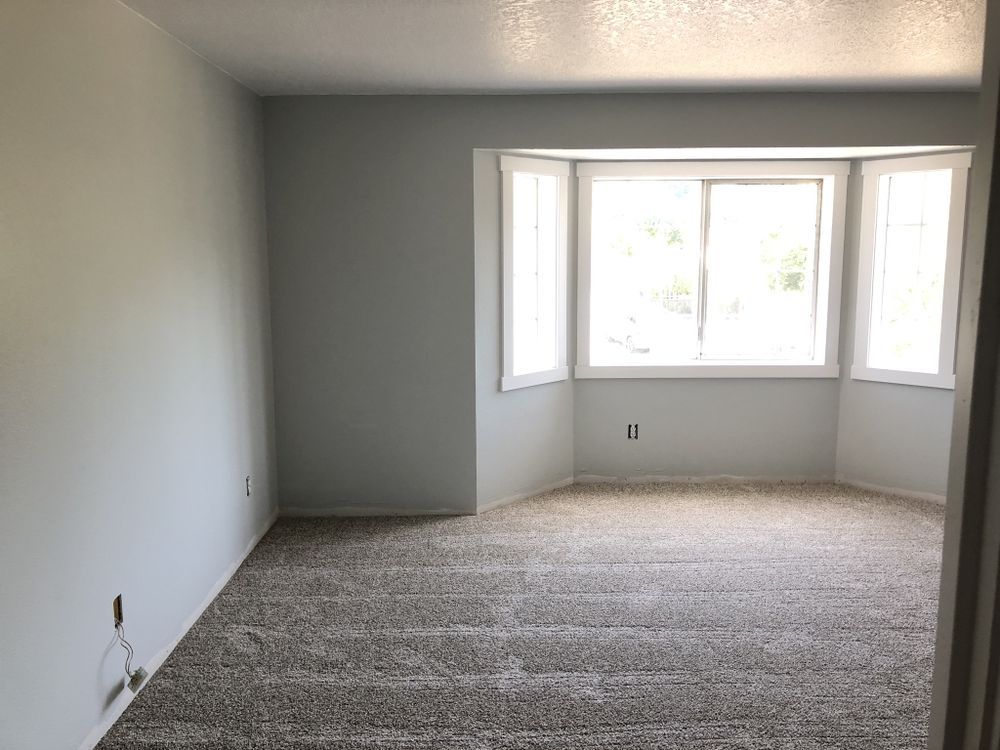 An empty living room with a bay window and carpet.