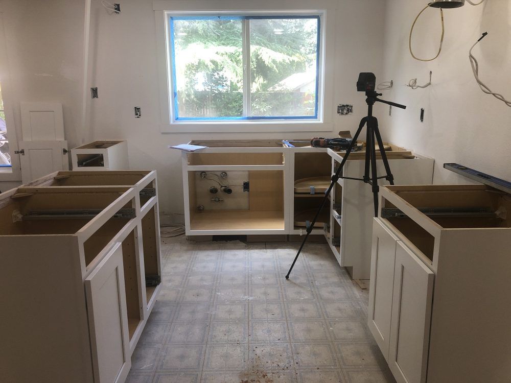 A kitchen under construction with white cabinets and a camera on a tripod.