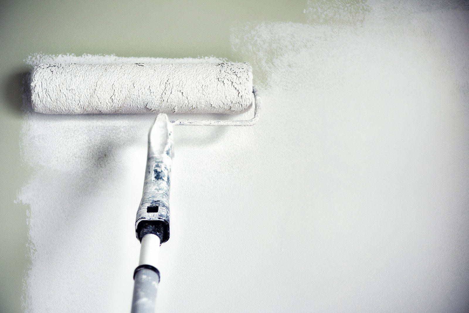 A paint roller is being used to paint a wall white.