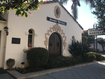A cream-colored building with a dark wooden arched door and a sign reading 